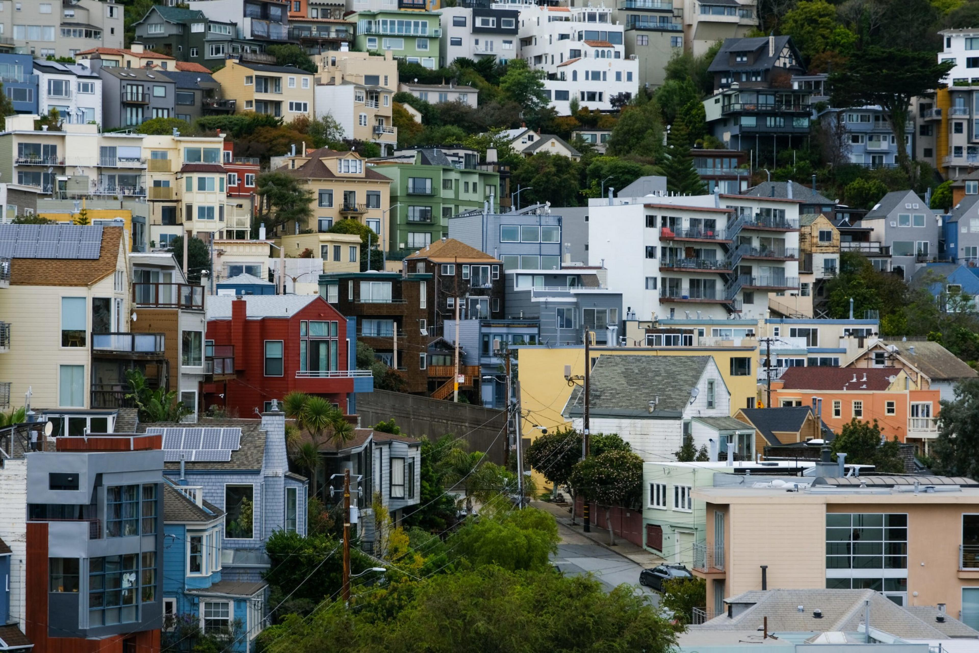 The image shows a vibrant hillside densely packed with colorful, modern houses and buildings. The architecture varies, and greenery speckles the scene.