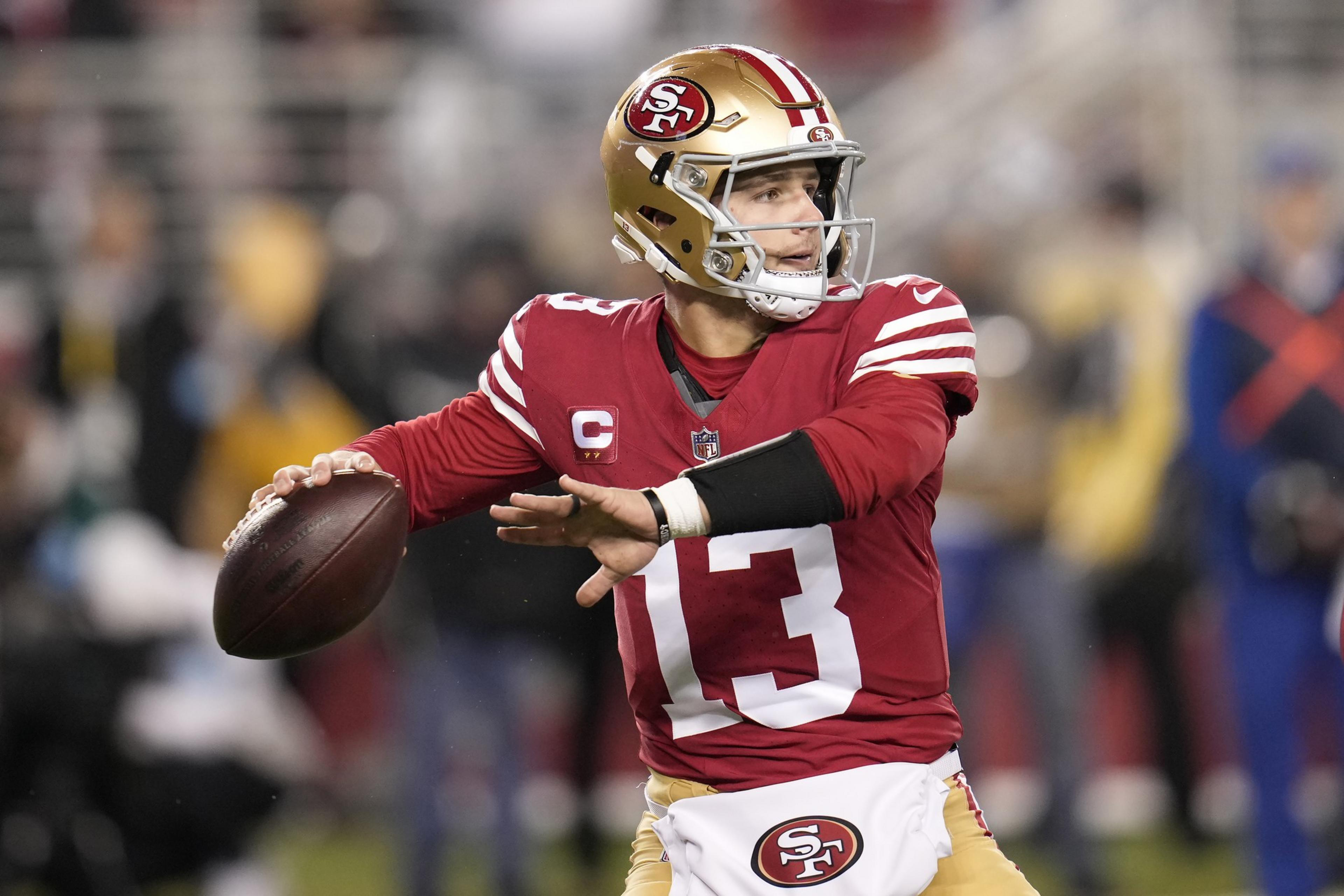 A football player in a red and gold uniform, number 13, is poised to throw the ball. He wears a helmet and a left arm sleeve, with a focused expression.