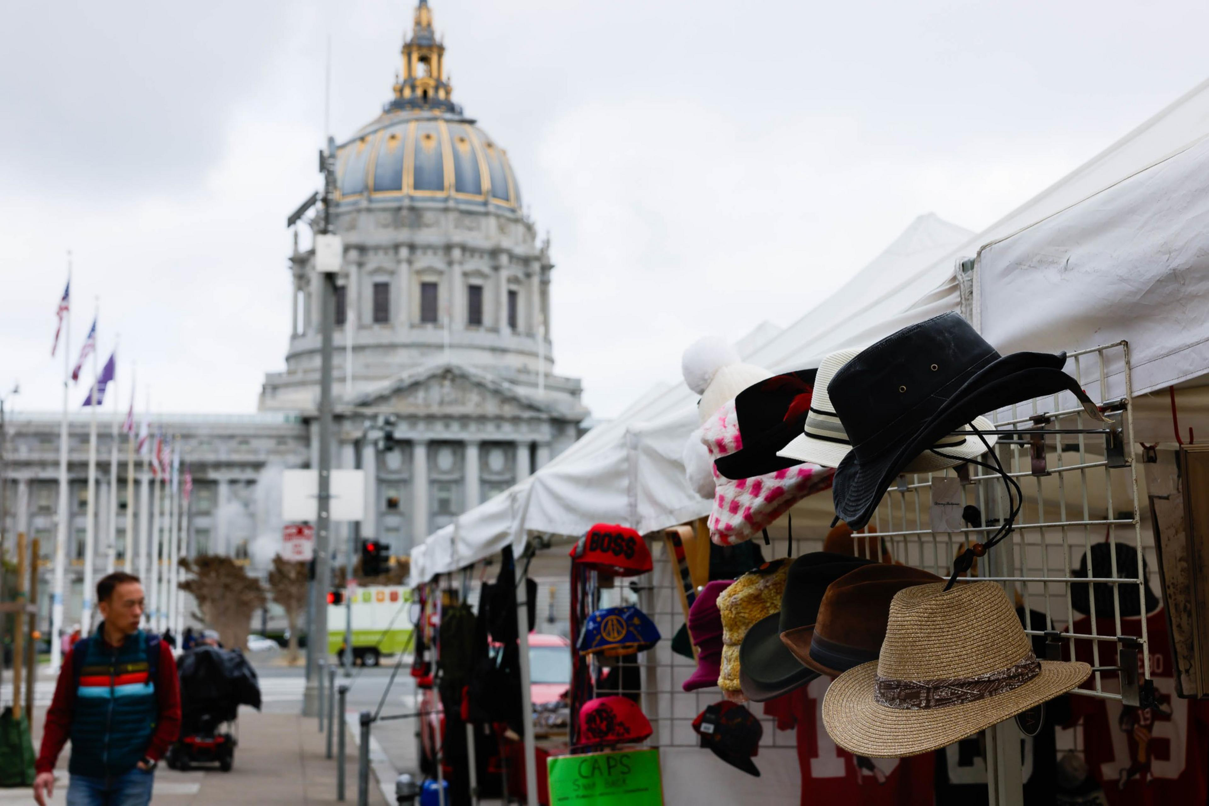 city hall's rotunda is visible on a gray day behind racks of merchandise being sold under white canopies