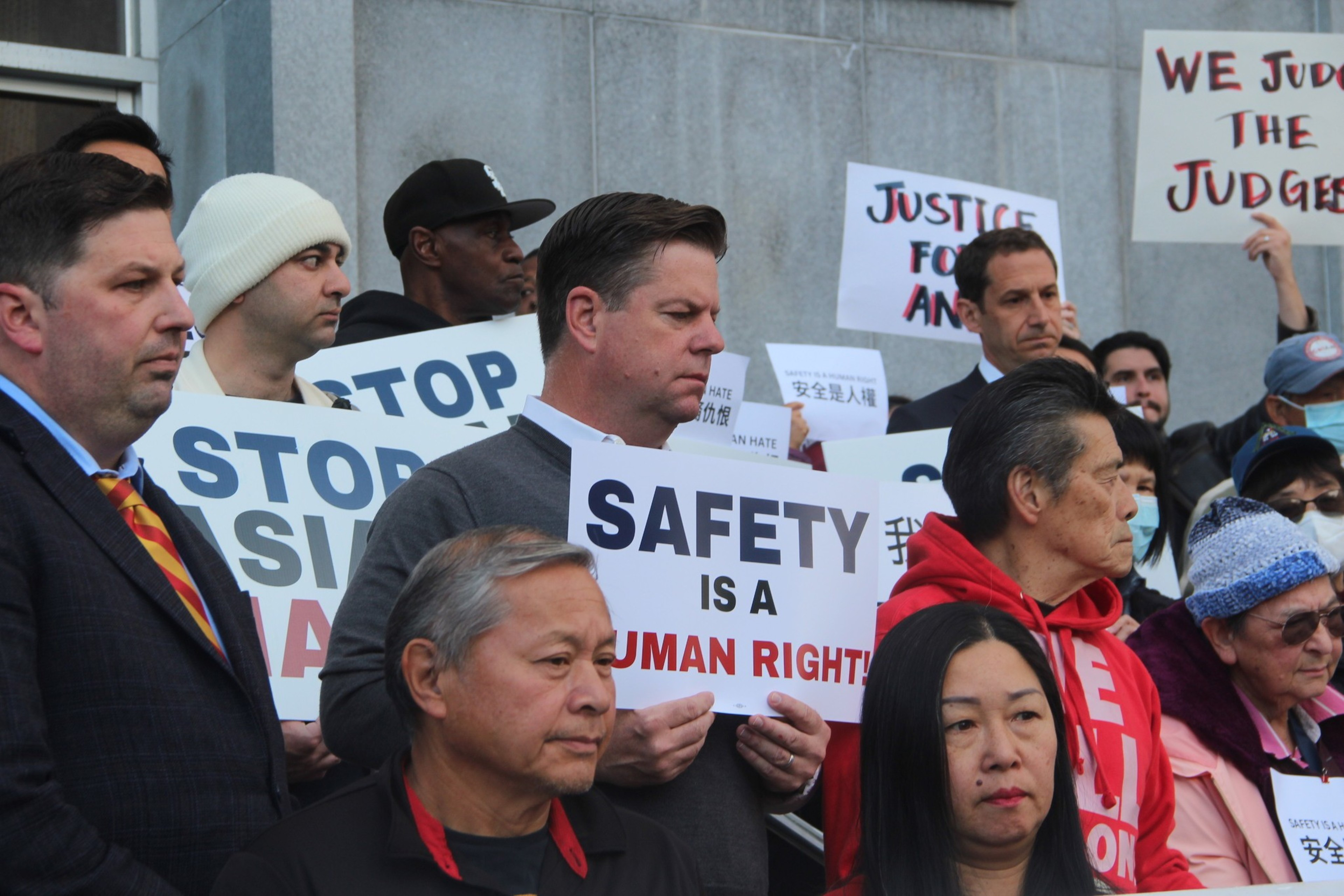 A group of people holding protest signs, one reads &quot;SAFETY IS A HUMAN RIGHT&quot;.