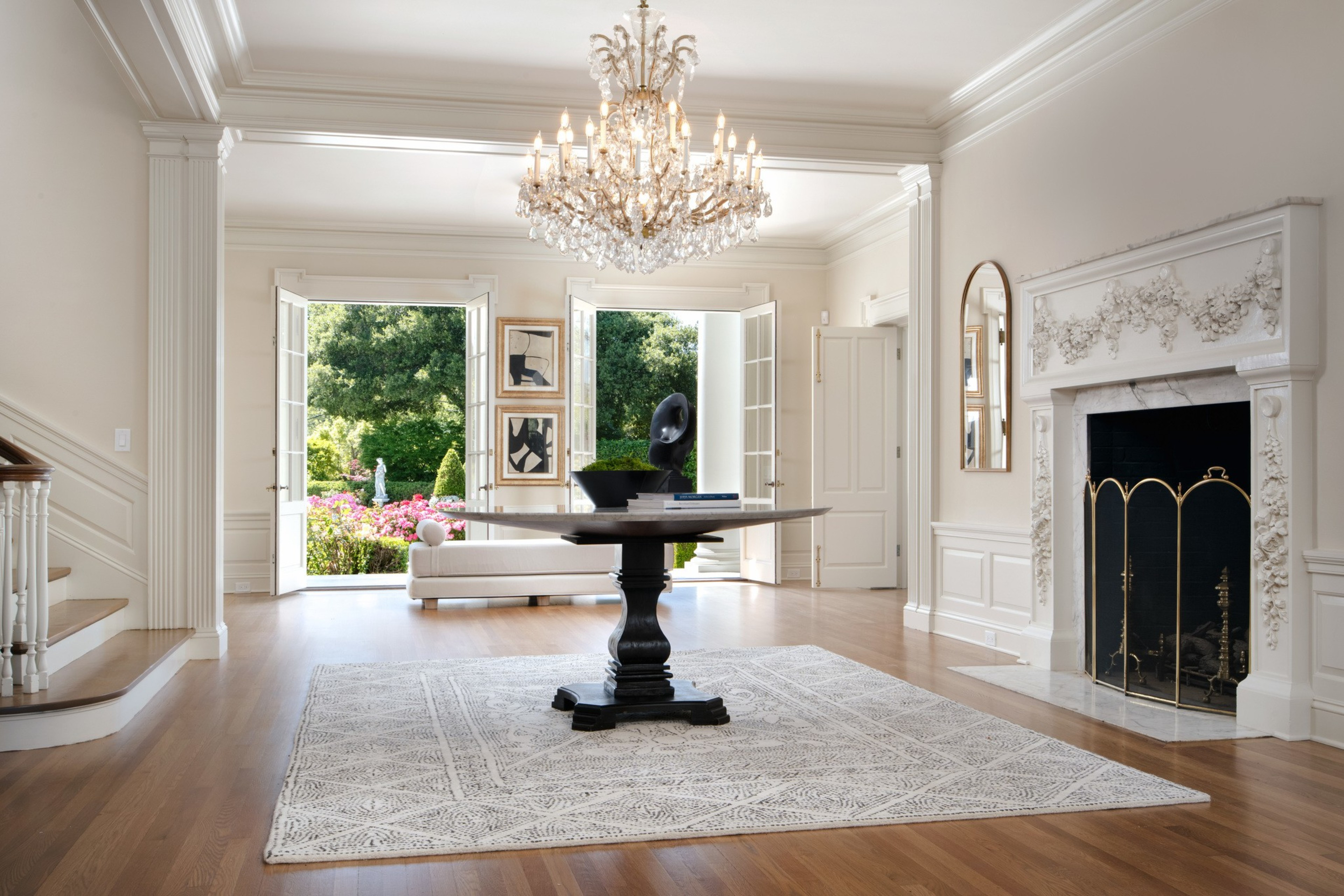 A chandelier hangs over a wooden-floored interior atrium with a fireplace at an estate