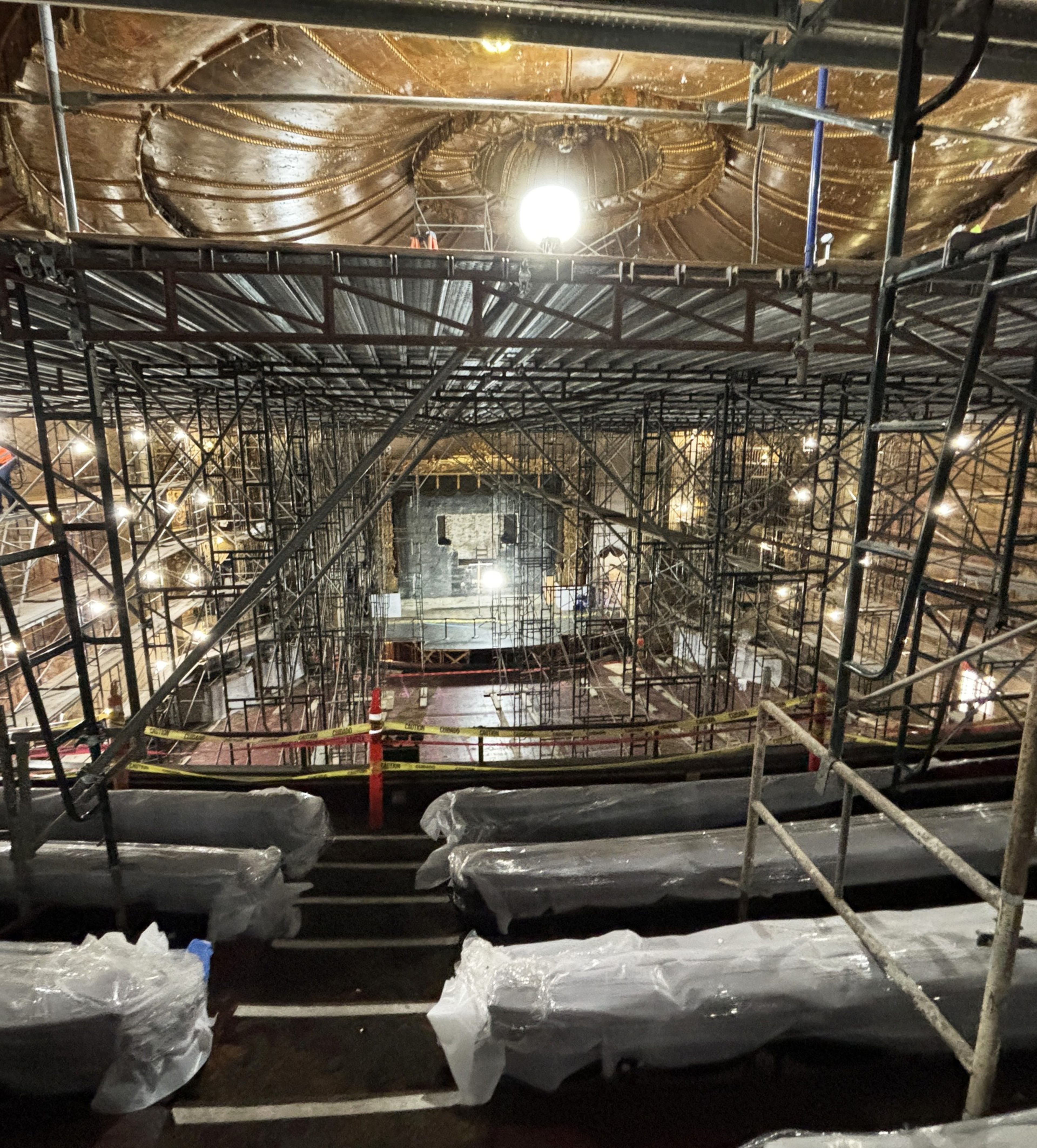 a zoomed-out shot of plastic-covered theater balcony seats with a giant scaffolding in the background