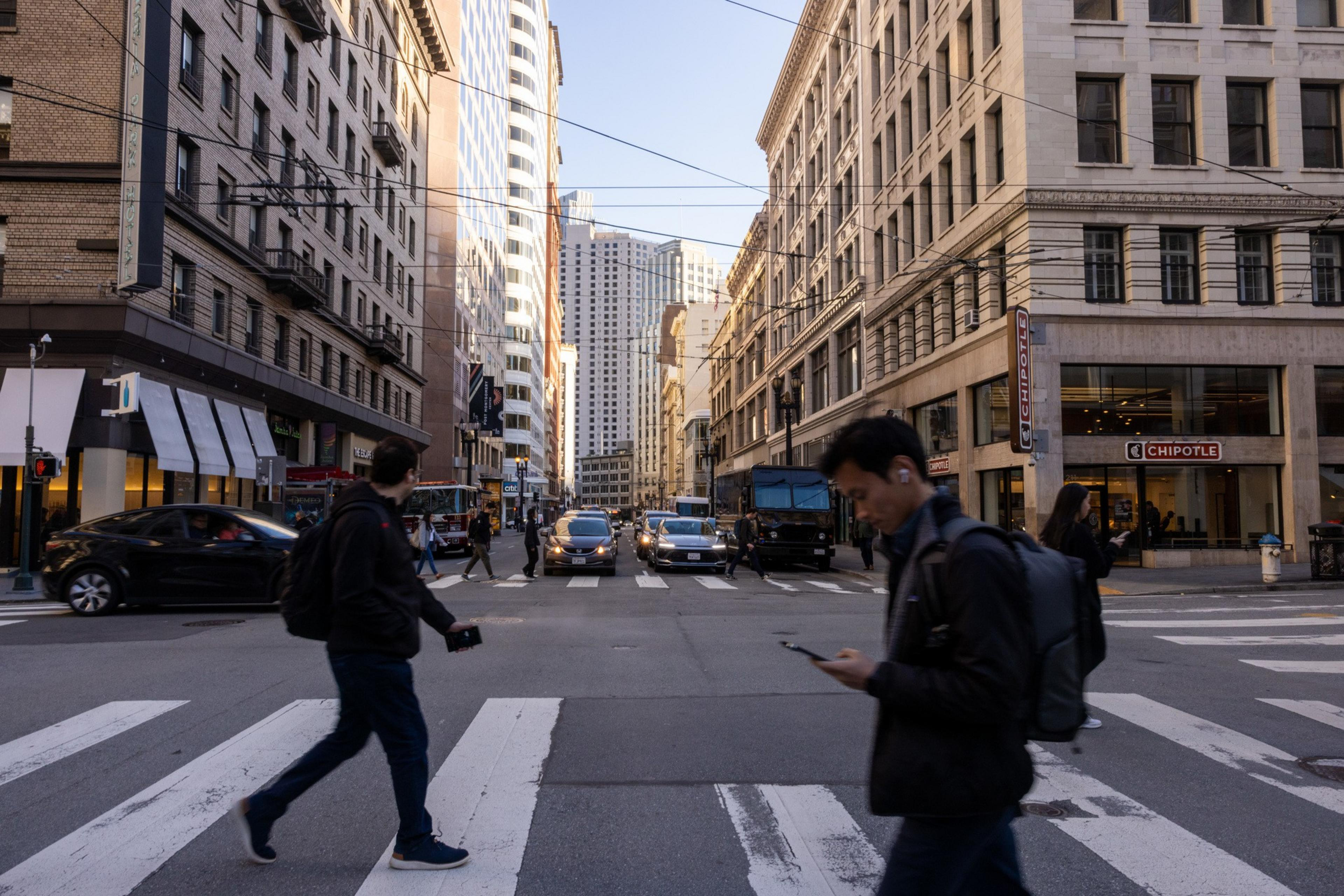 A busy city street with pedestrians crossing, cars in traffic, tall buildings,.