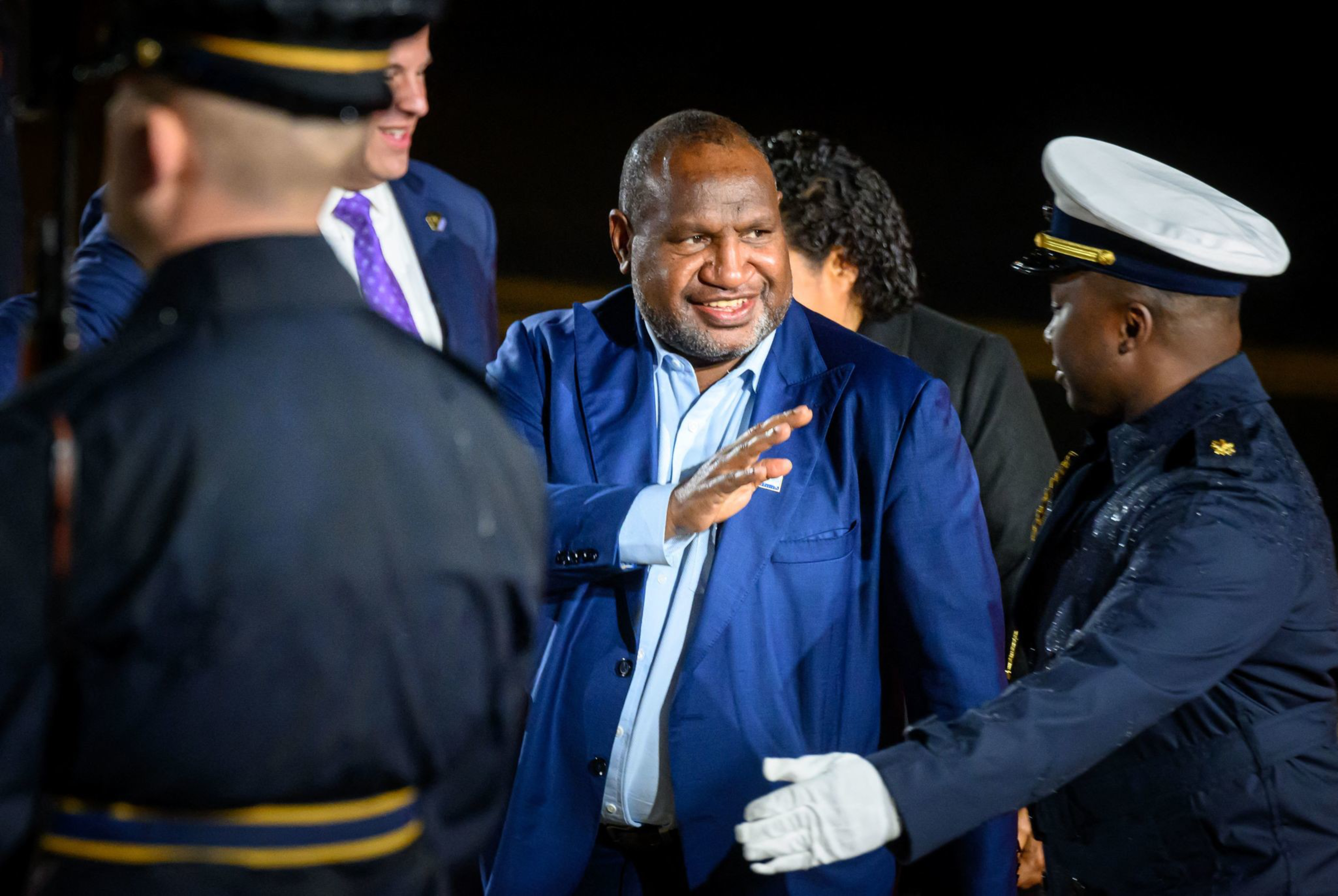 Papua New Guinea's Prime Minister James Marape waves into the distance while walking between members of security personnel.