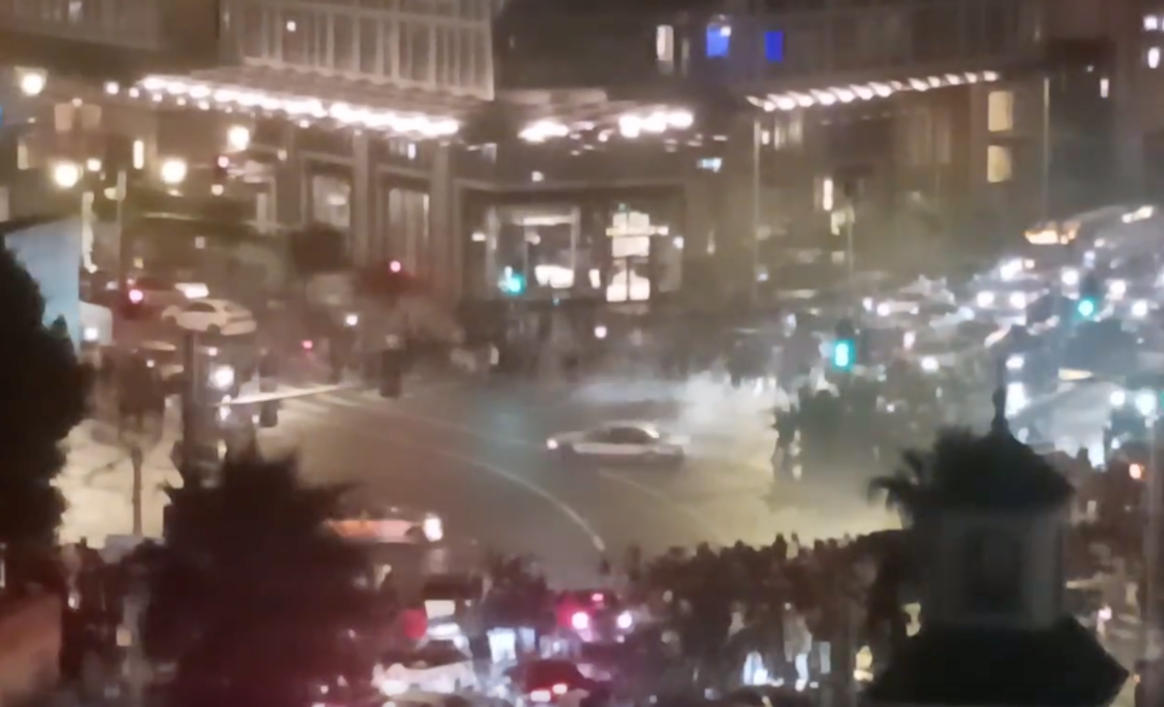 a car is seen in an intersection surrounded by a crowd of people from a distance