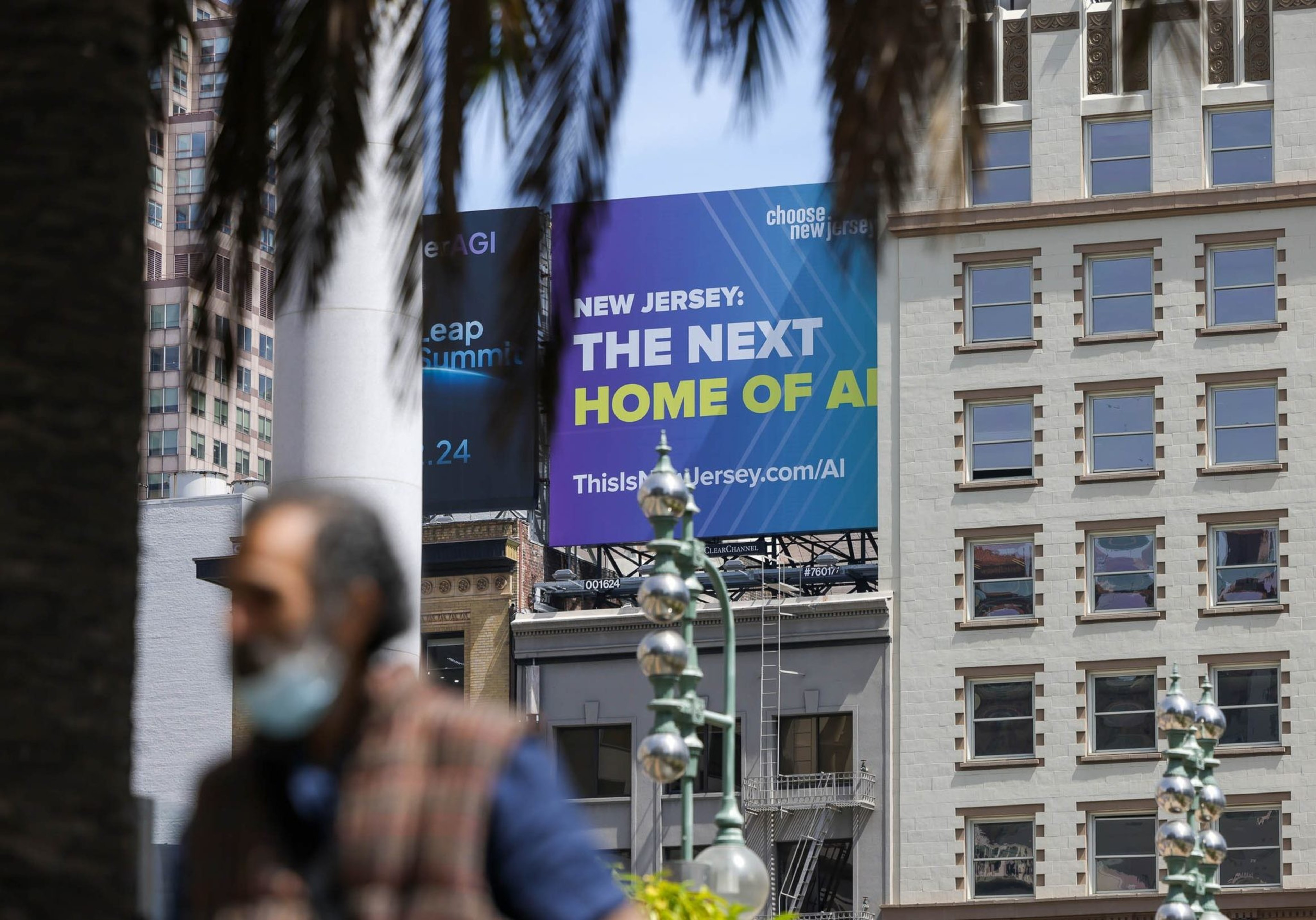 Urban scene with blurred foreground figures, palm trees, a building backdrop, and a billboard promoting New Jersey as "The Next Home of AI."