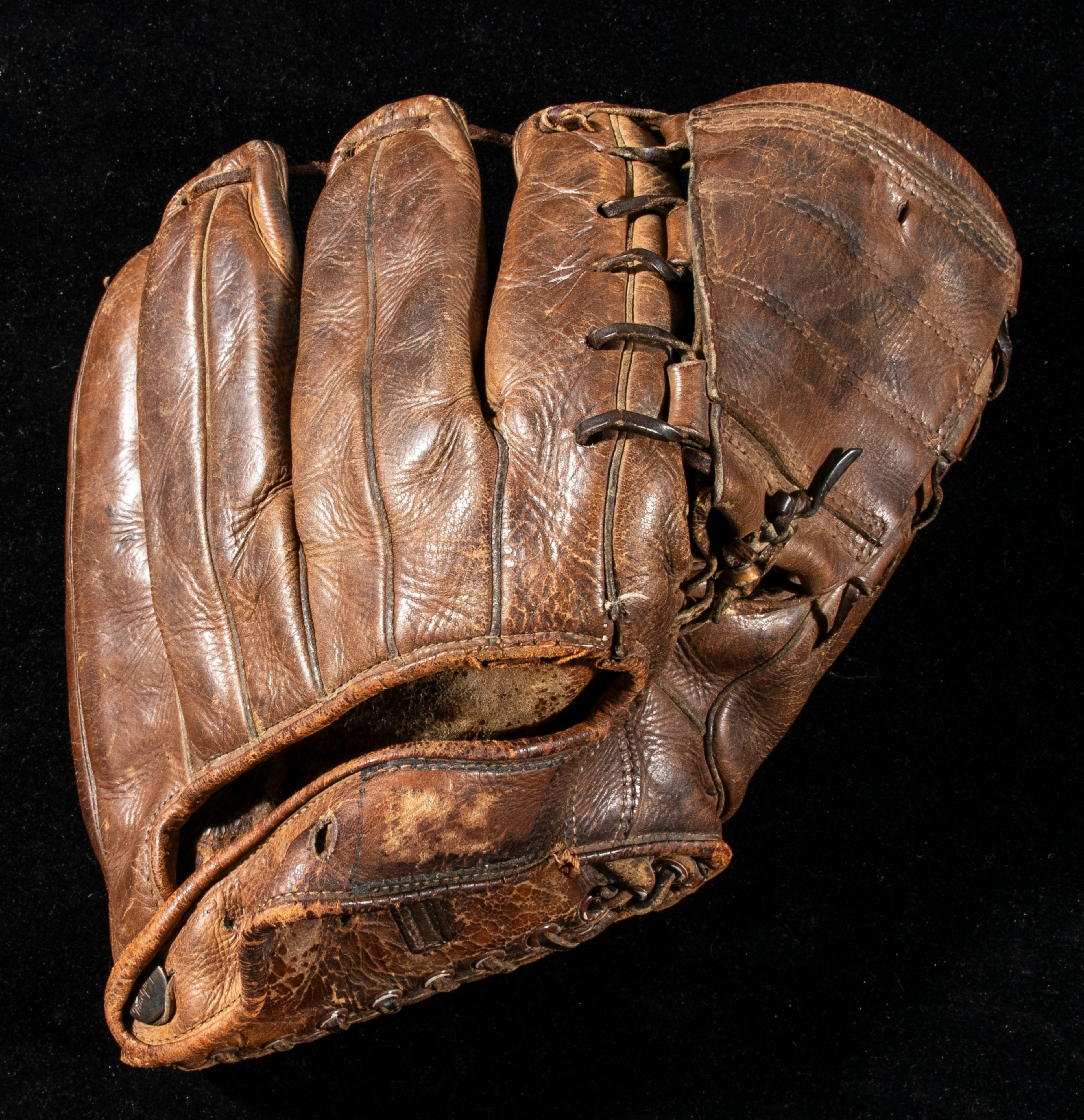 The image shows a worn brown leather baseball glove with visible stitching and laces against a black background.