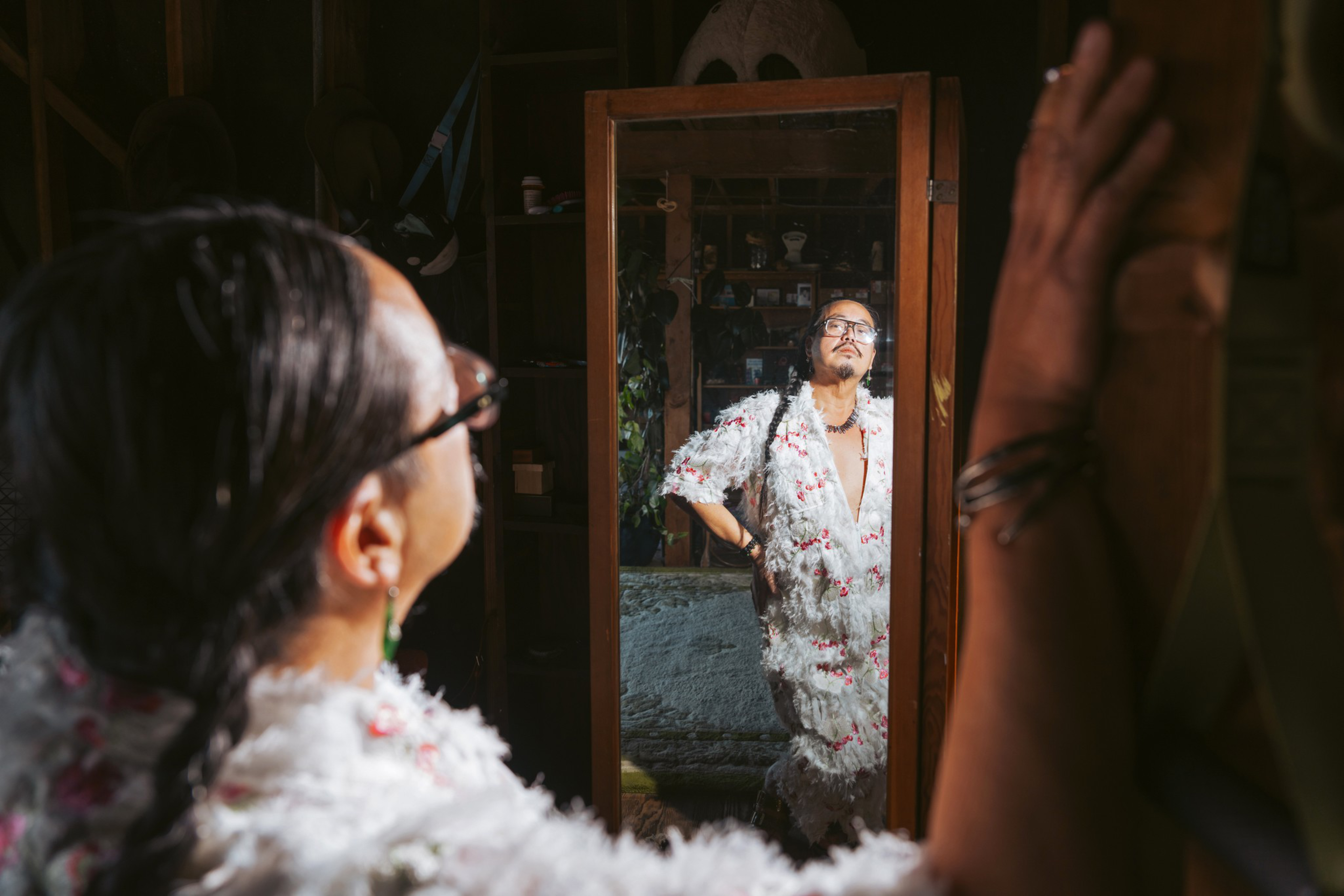 A person looks at themselves in a mirror, wearing a fluffy, textured white and red outfit. The reflection shows them with a hand on their hip in a dimly lit room.