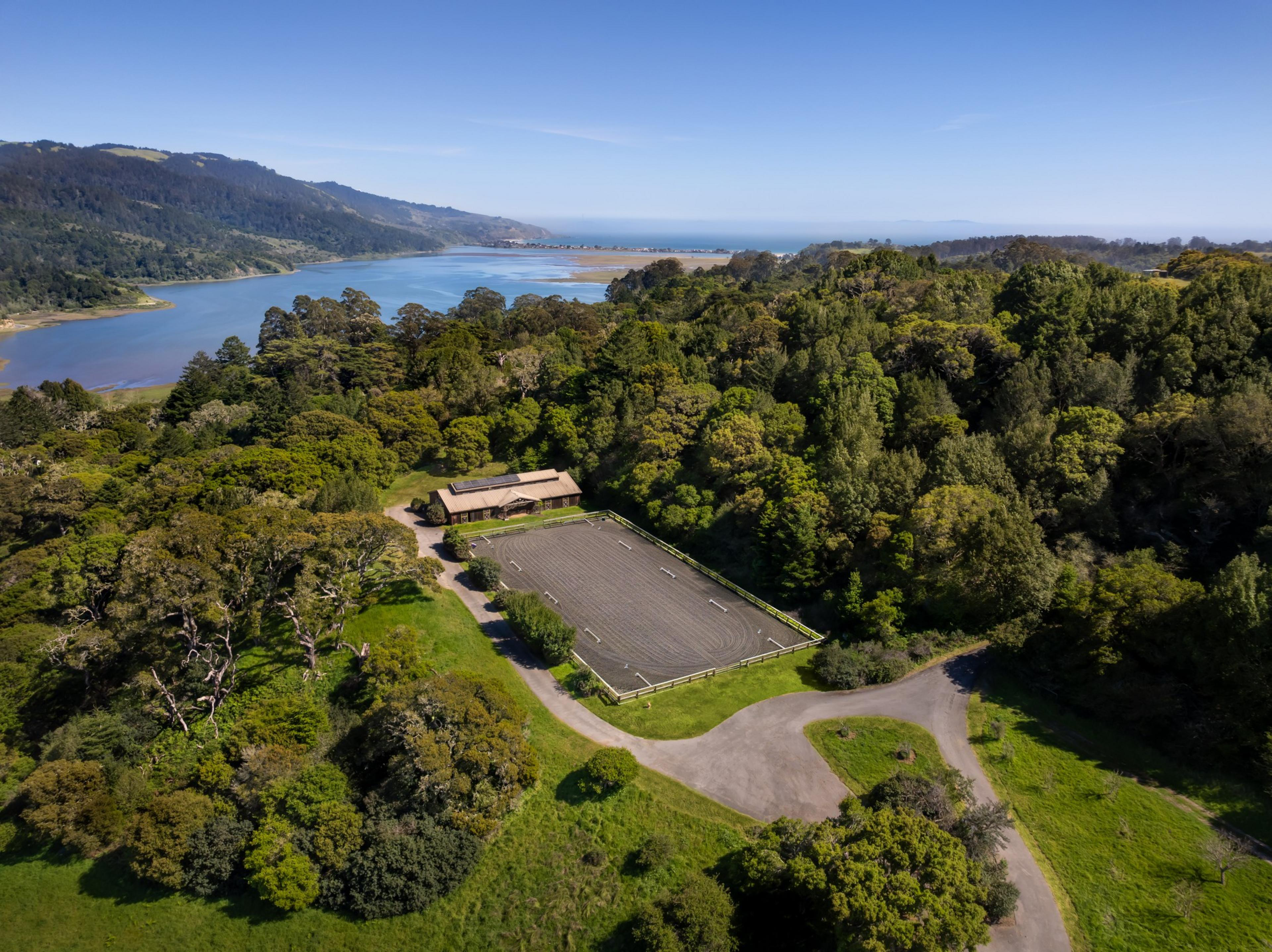 Aerial view of a parking lot next to a building, amidst green forest and near a coastline.
