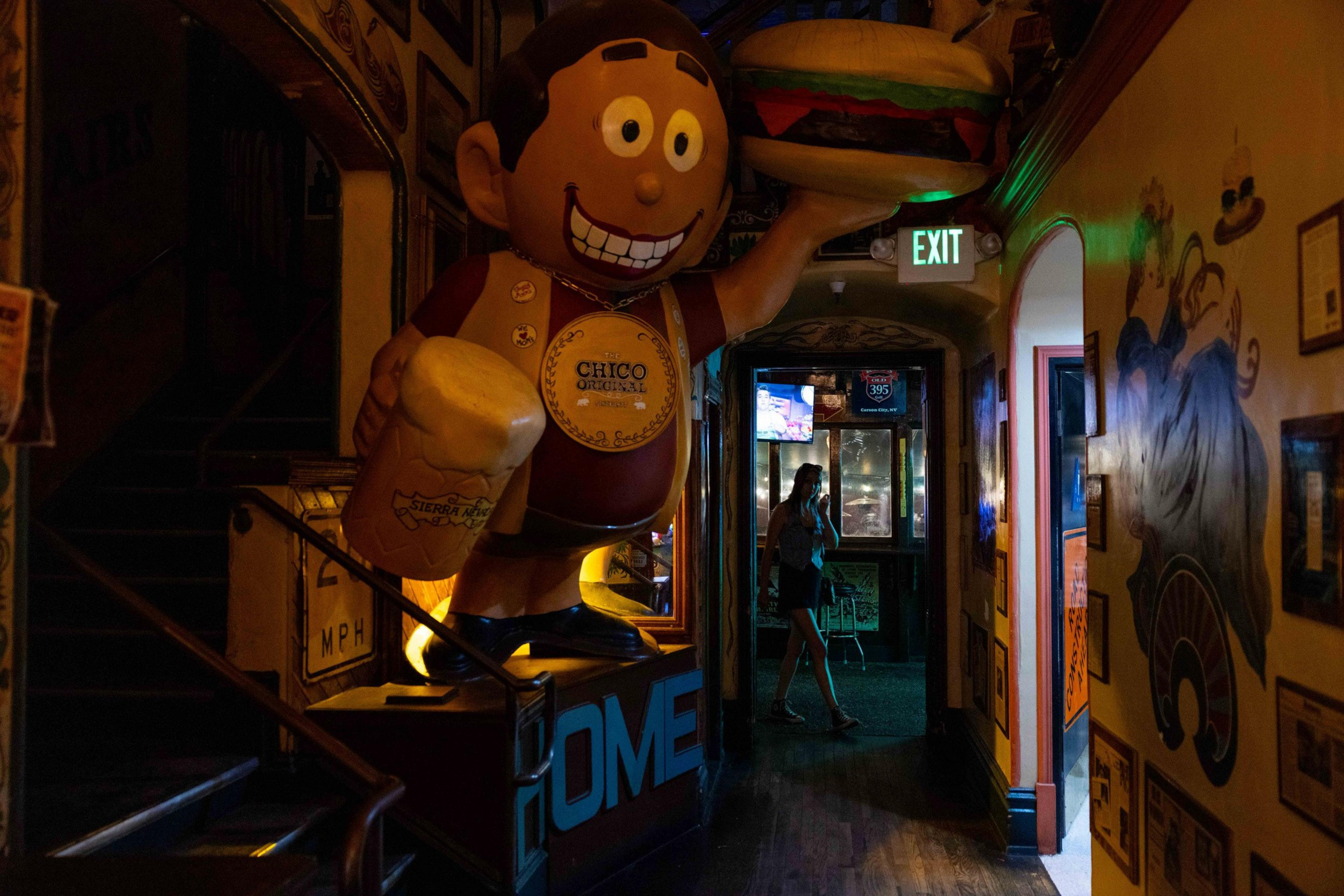 A large cartoon figure holds a burger and a mug labeled &quot;Sierra Nevada&quot; in a dimly lit corridor. A person stands near a glowing exit sign.
