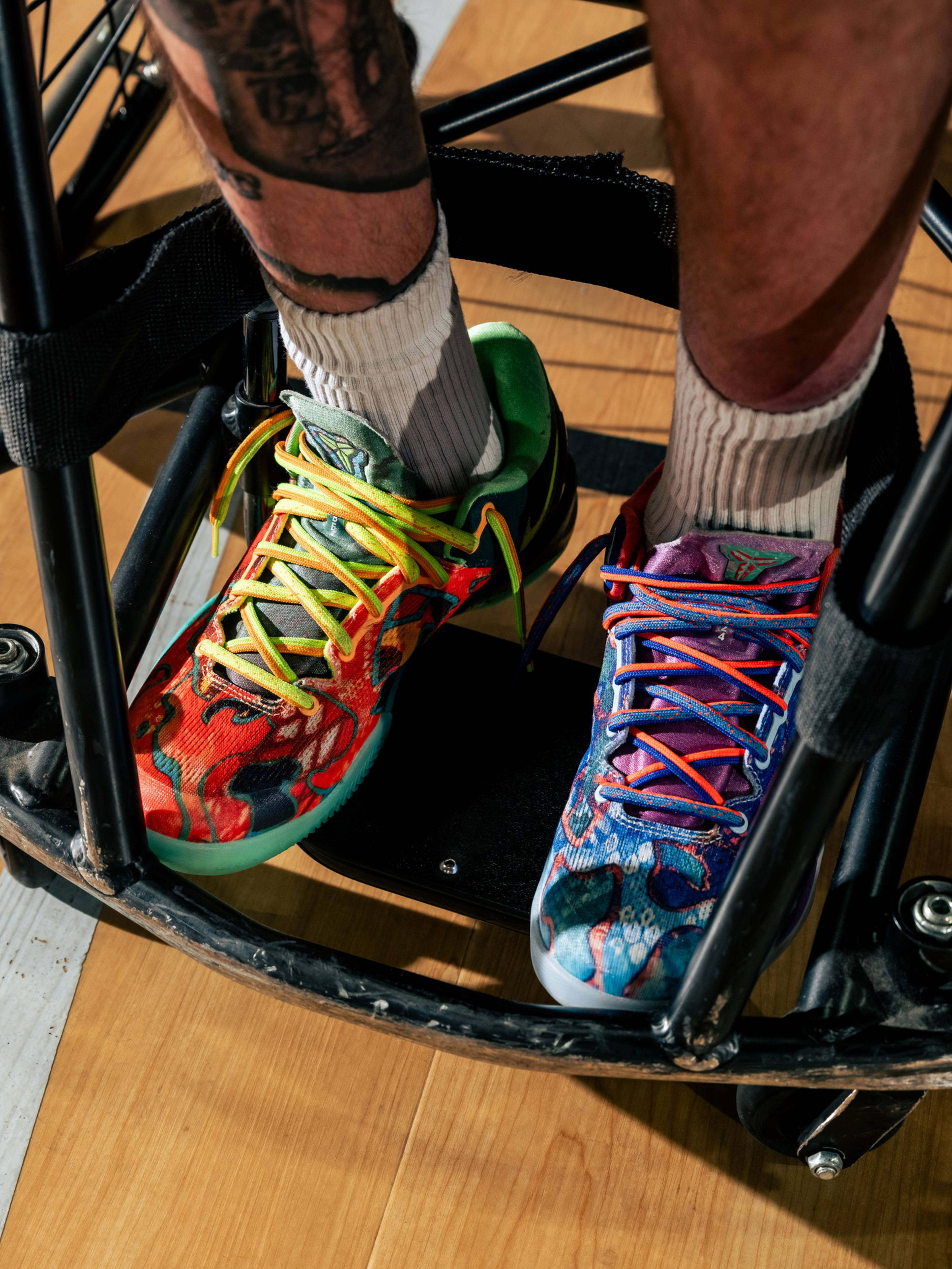 A pair of colorful, mismatched sneakers with vibrant designs and different colored laces worn by a person seated in a wheelchair.