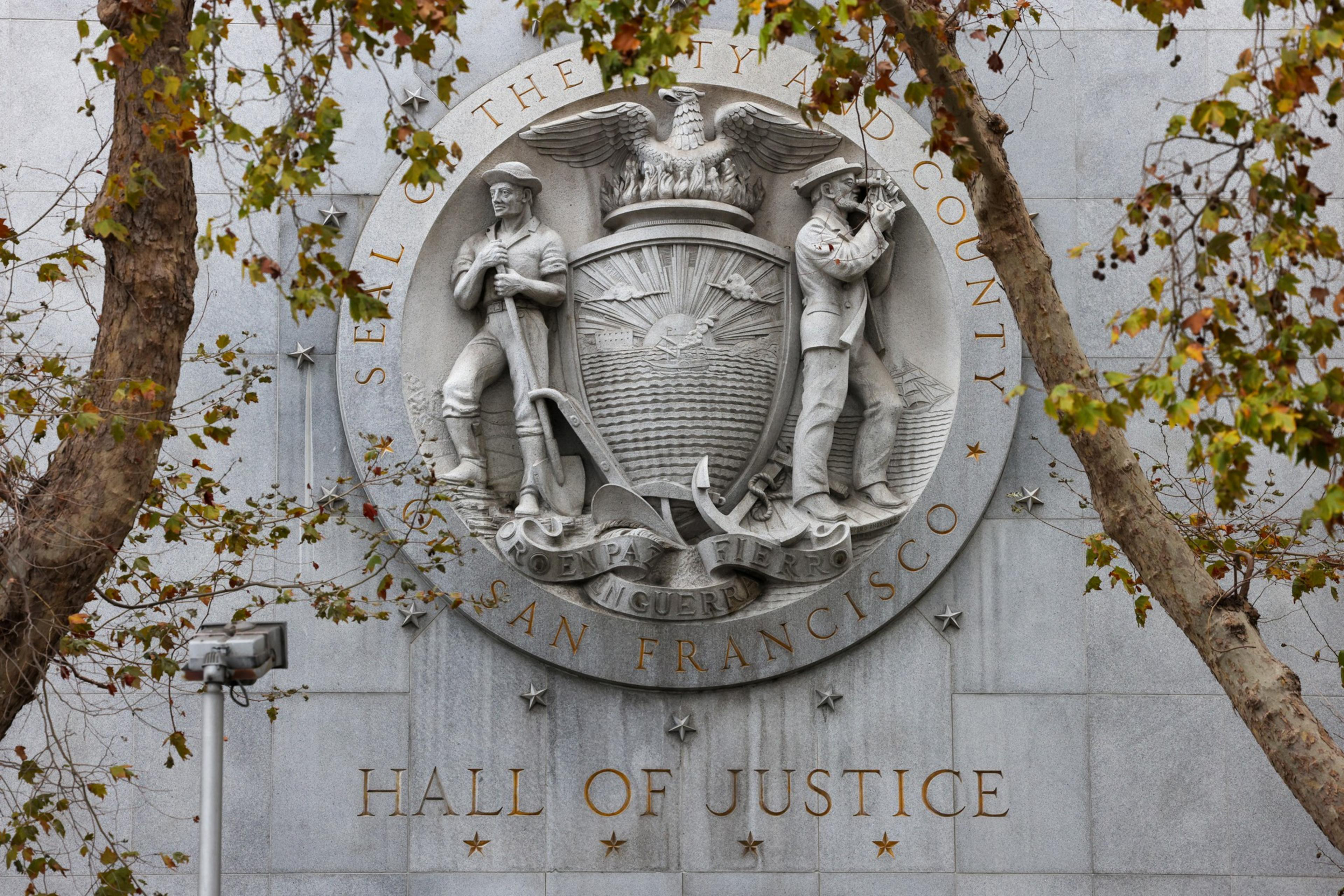 A stone seal of San Francisco County features a miner and a sailor holding tools, with an eagle above and "Hall of Justice" engraved below.