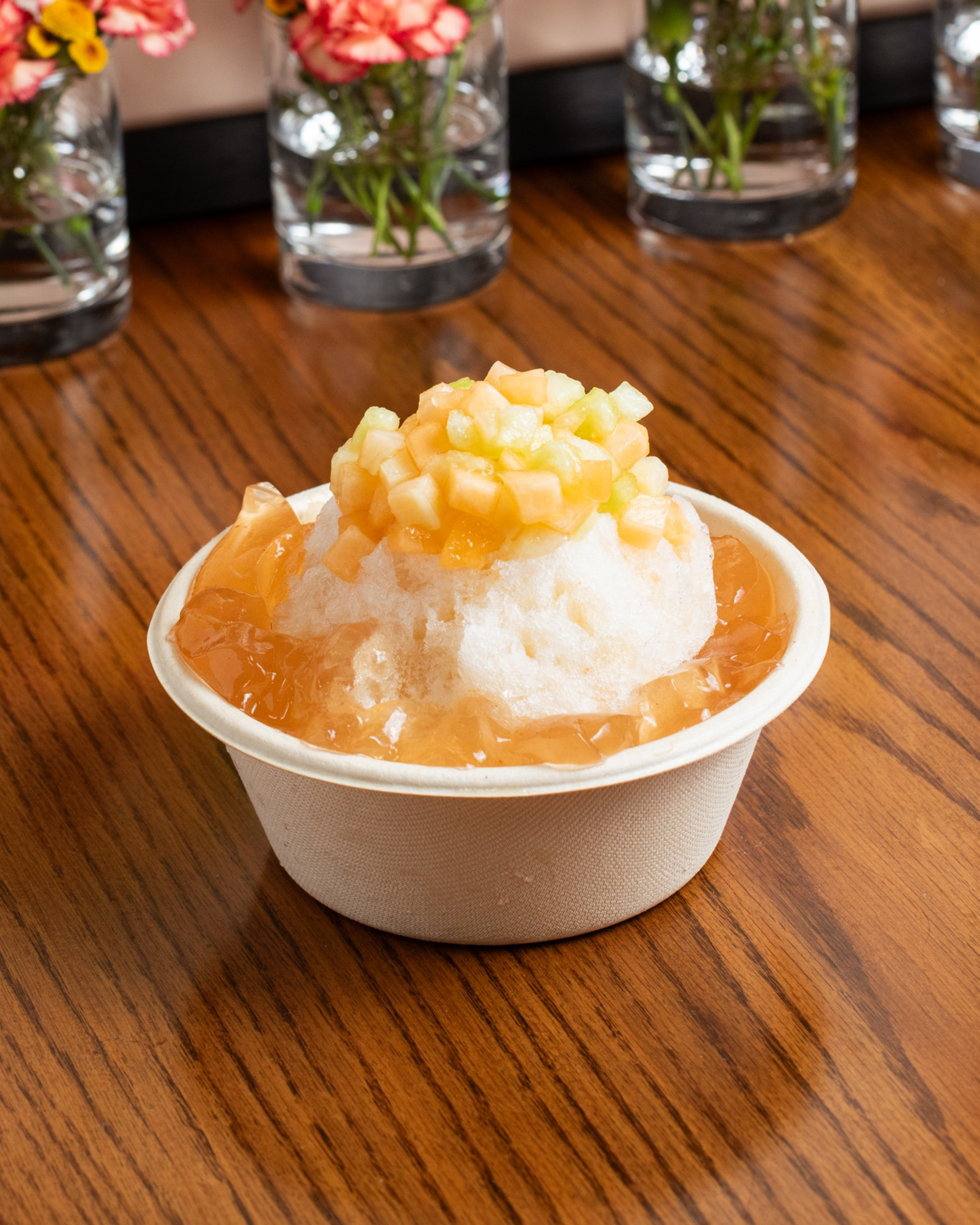 A bowl of shave ice with cut fruit and jelly on top.