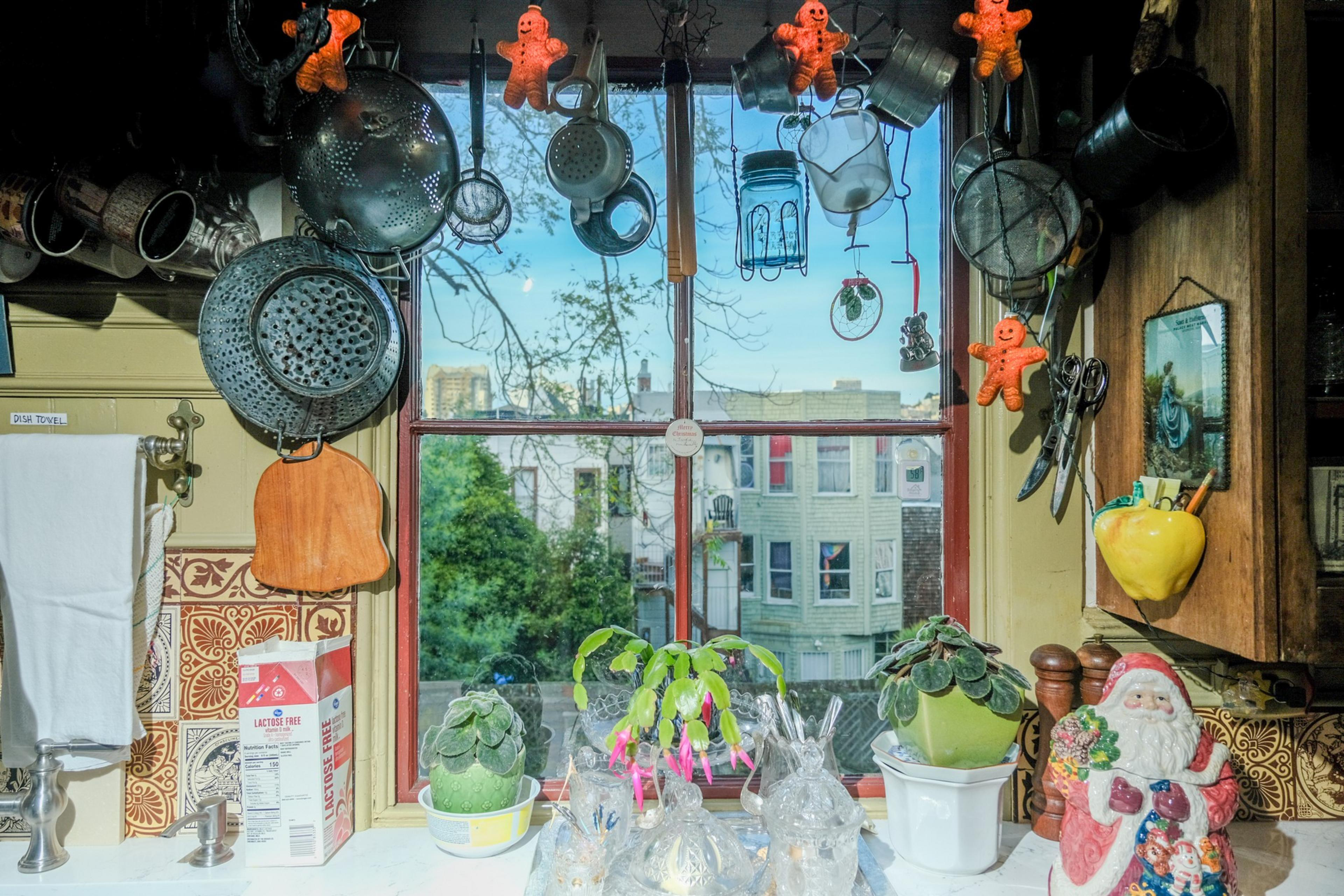 A window facing the street with pots, flowers, and a little Santa on the coutner.