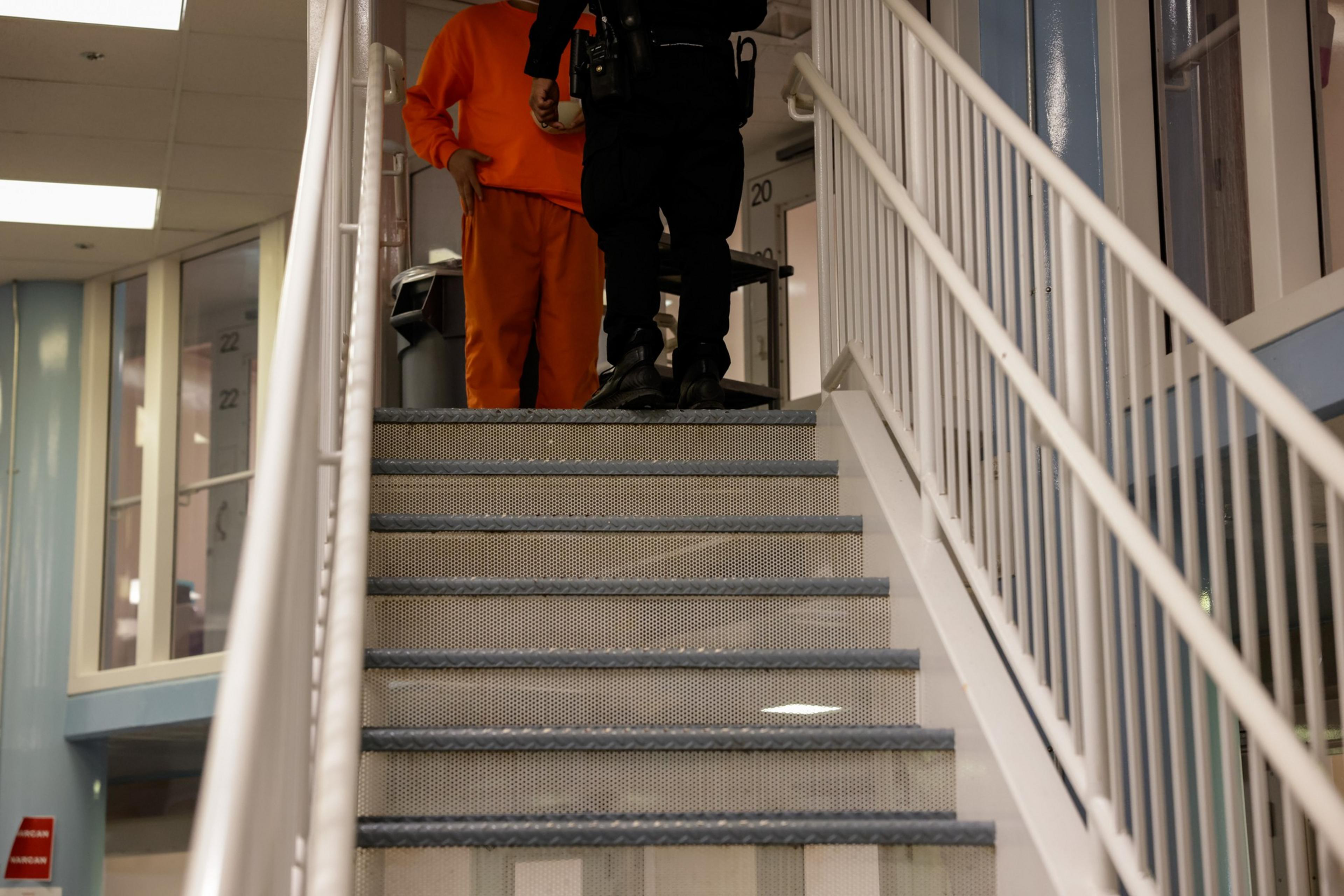 An inmate and a sheriff's deputy approach a staircase in the jail.