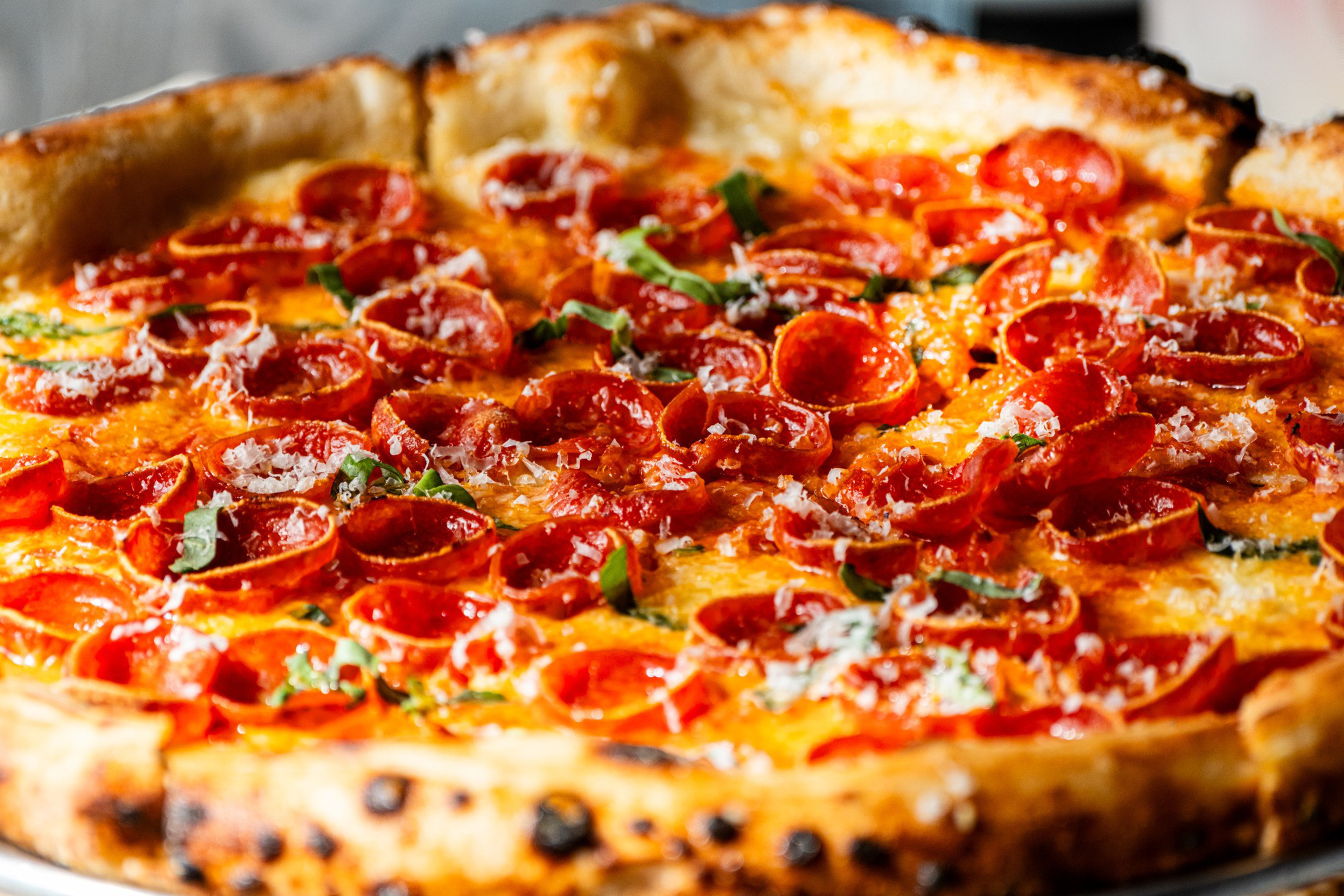 A pizza topped with crispy pepperoni slices, melted cheese, and garnished with fresh basil. The crust is golden-brown and slightly charred.