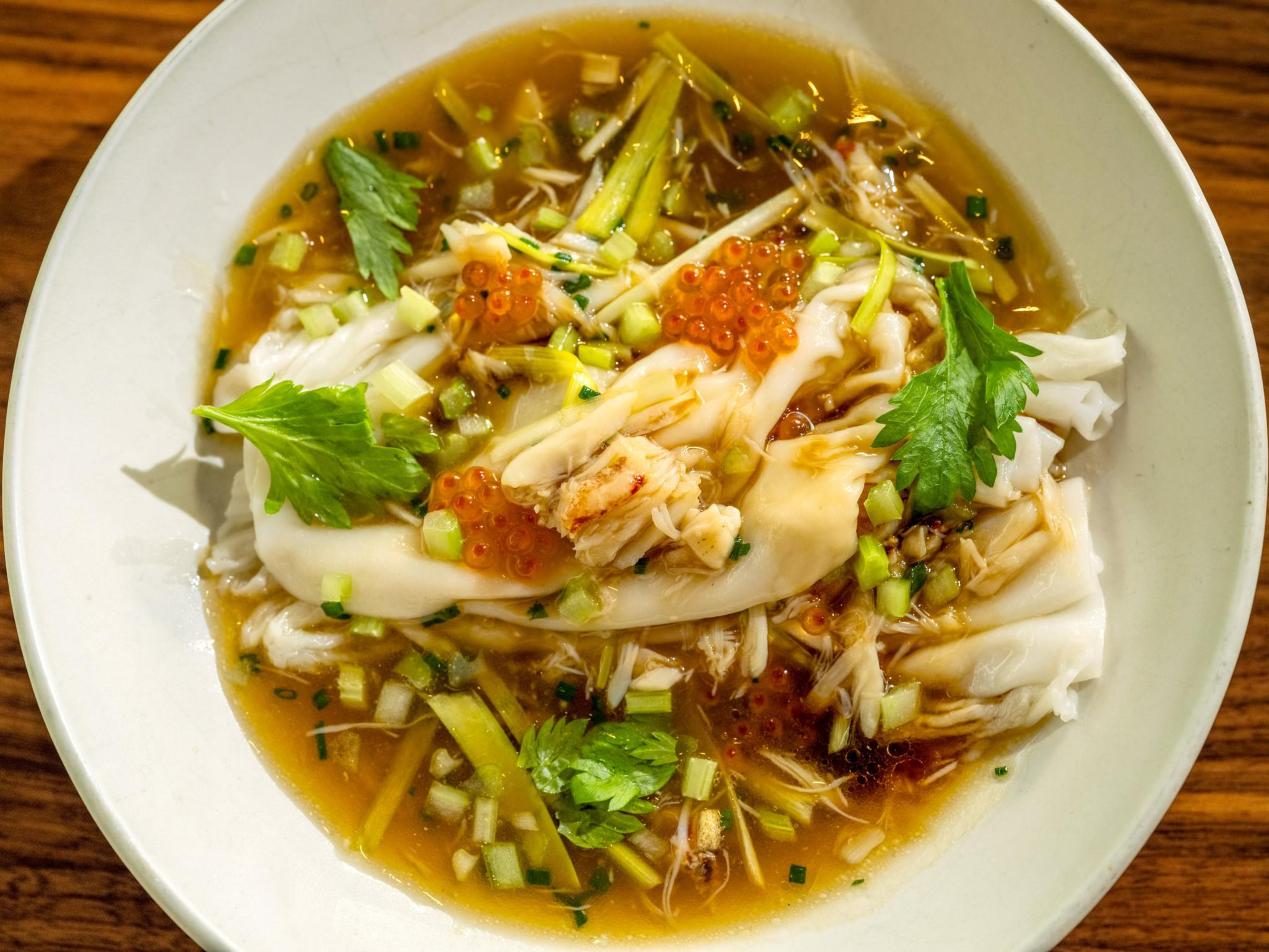 Rice noodle rolls topped with shredded chicken, herbs, and fish roe, served in a clear broth with chopped green onions.