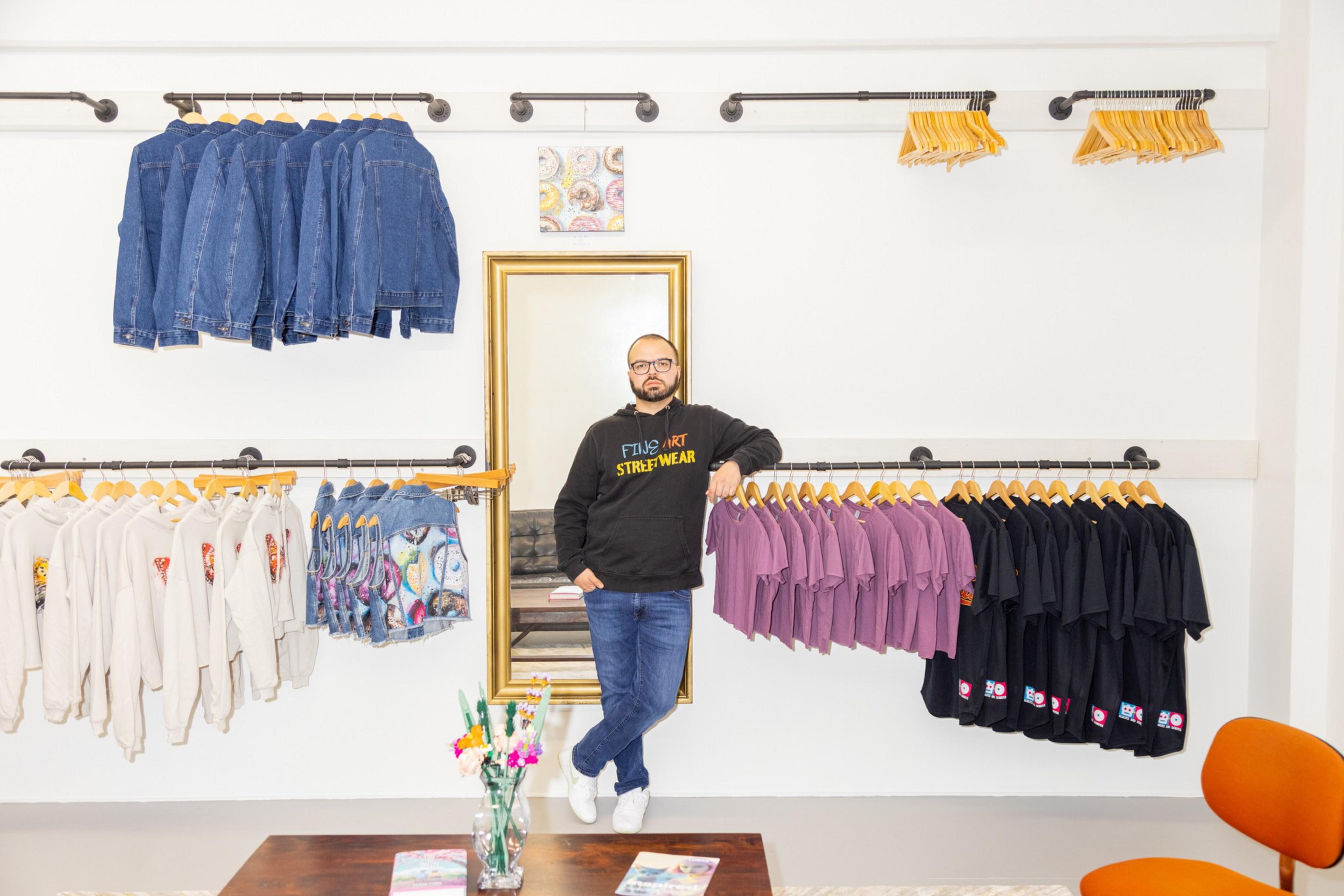 A man stands in a boutique with racks of clothing, jeans above, and shirts in neutral tones.