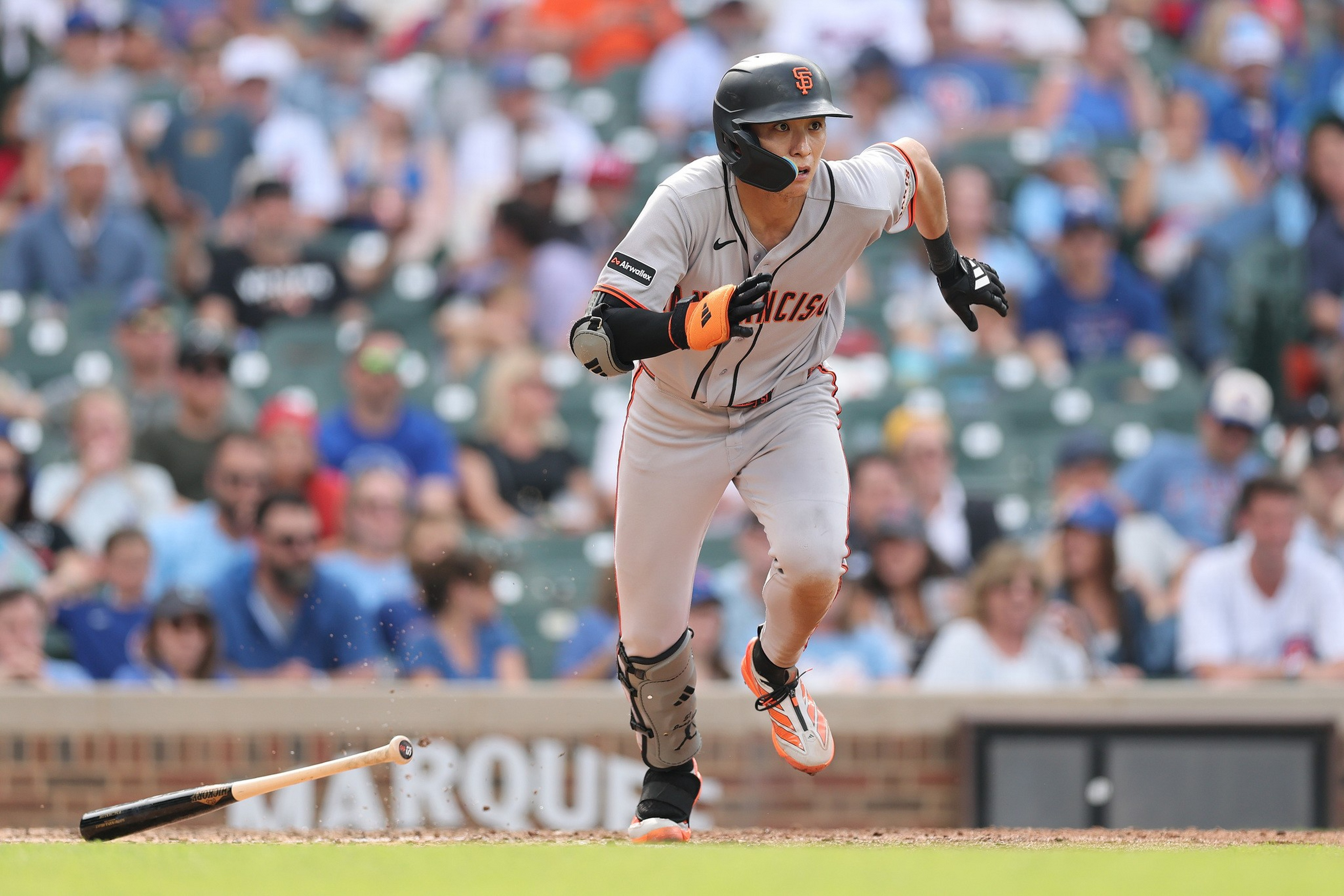 A baseball player in a San Francisco Giants uniform is sprinting after hitting, while the bat lies on the ground behind him.