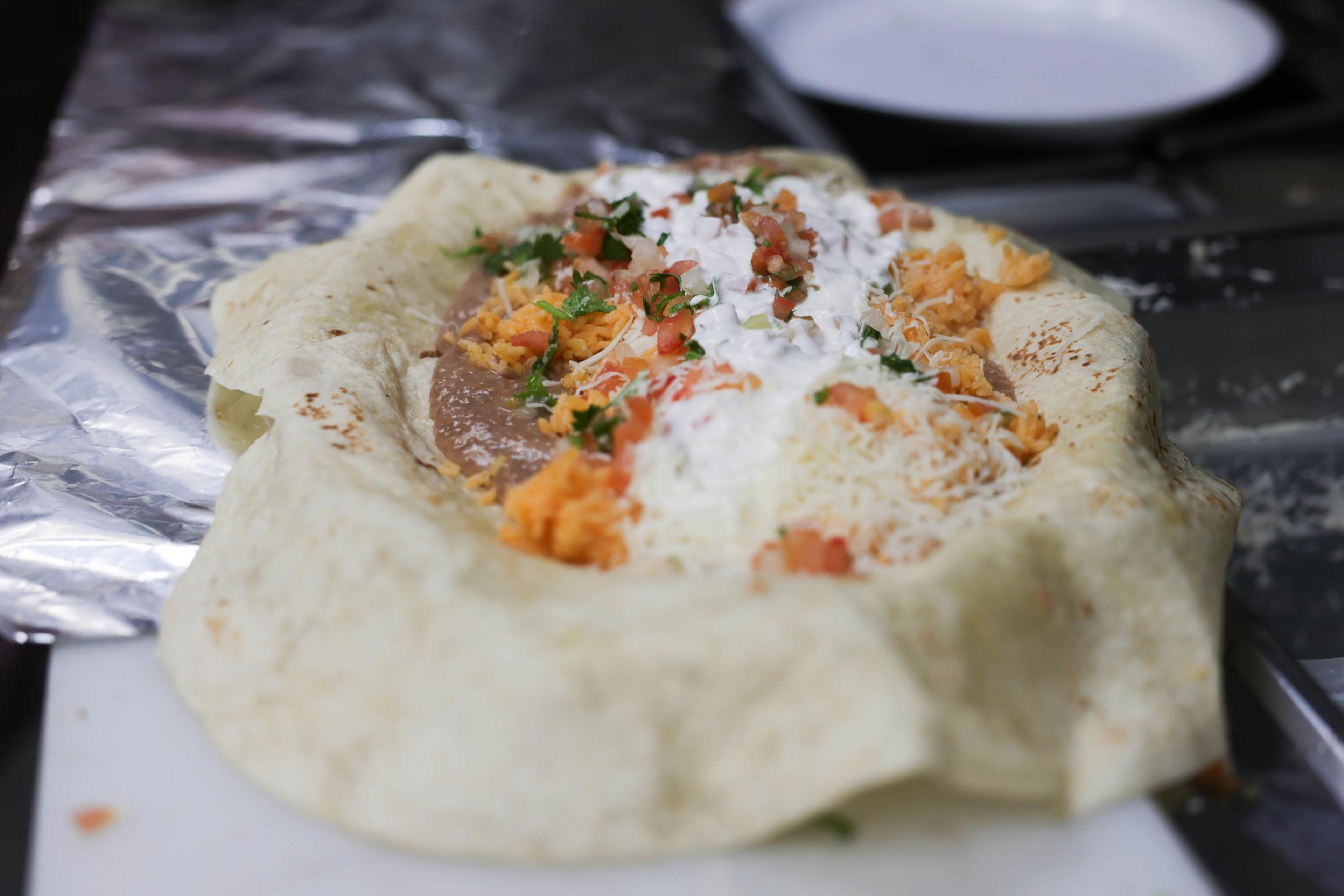 An open burrito with rice, beans, cheese, and sauce on foil.