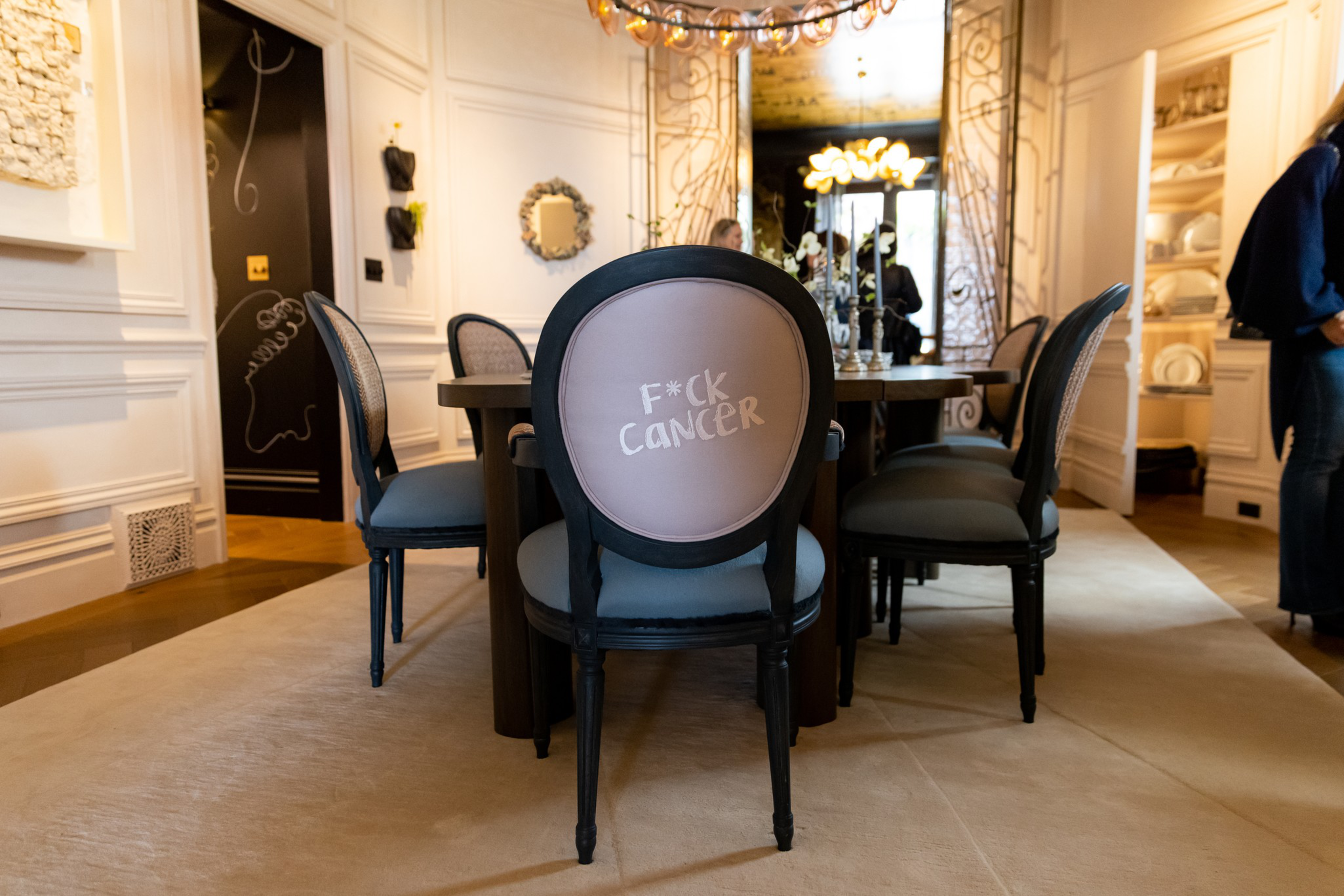 A dining room features a chair with the phrase “F*ck Cancer” written on its backrest in bold letters.