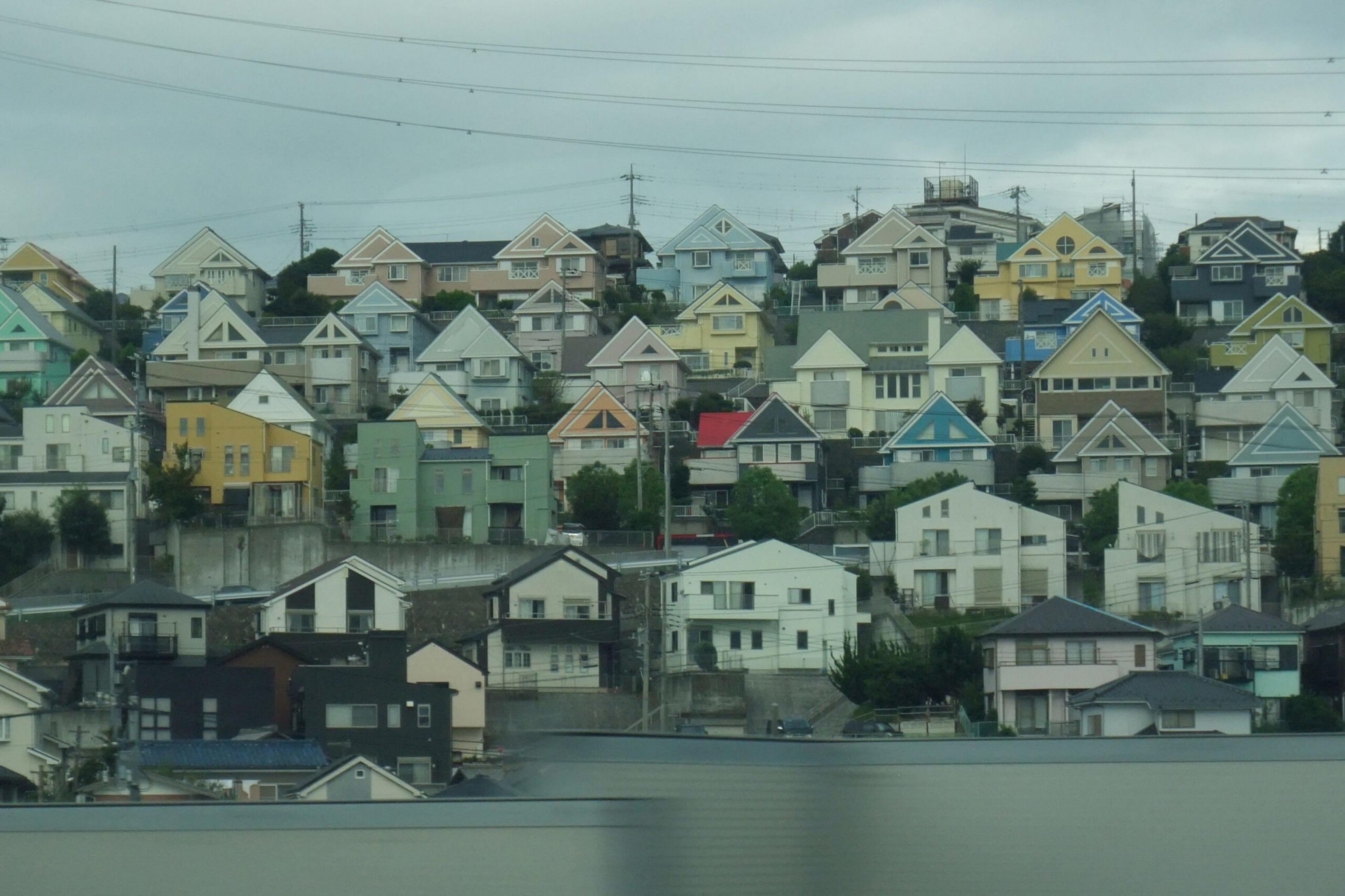 A hillside neighborhood with multiple small, colorful houses closely packed together, featuring triangular roofs under a cloudy sky.