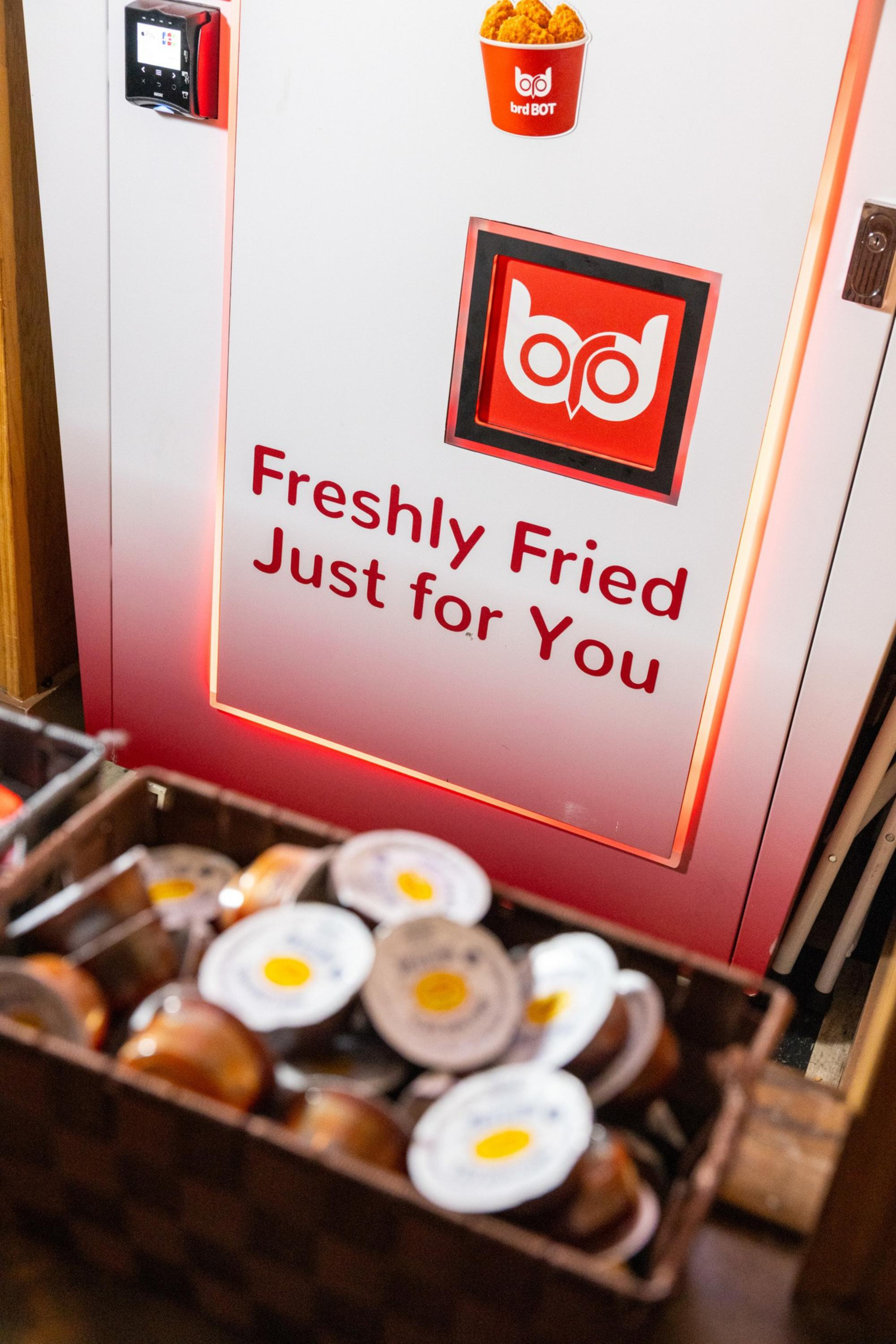 A vending machine with “Freshly Fried Just for You” text and an owl logo, next to a basket filled with sauce cups.
