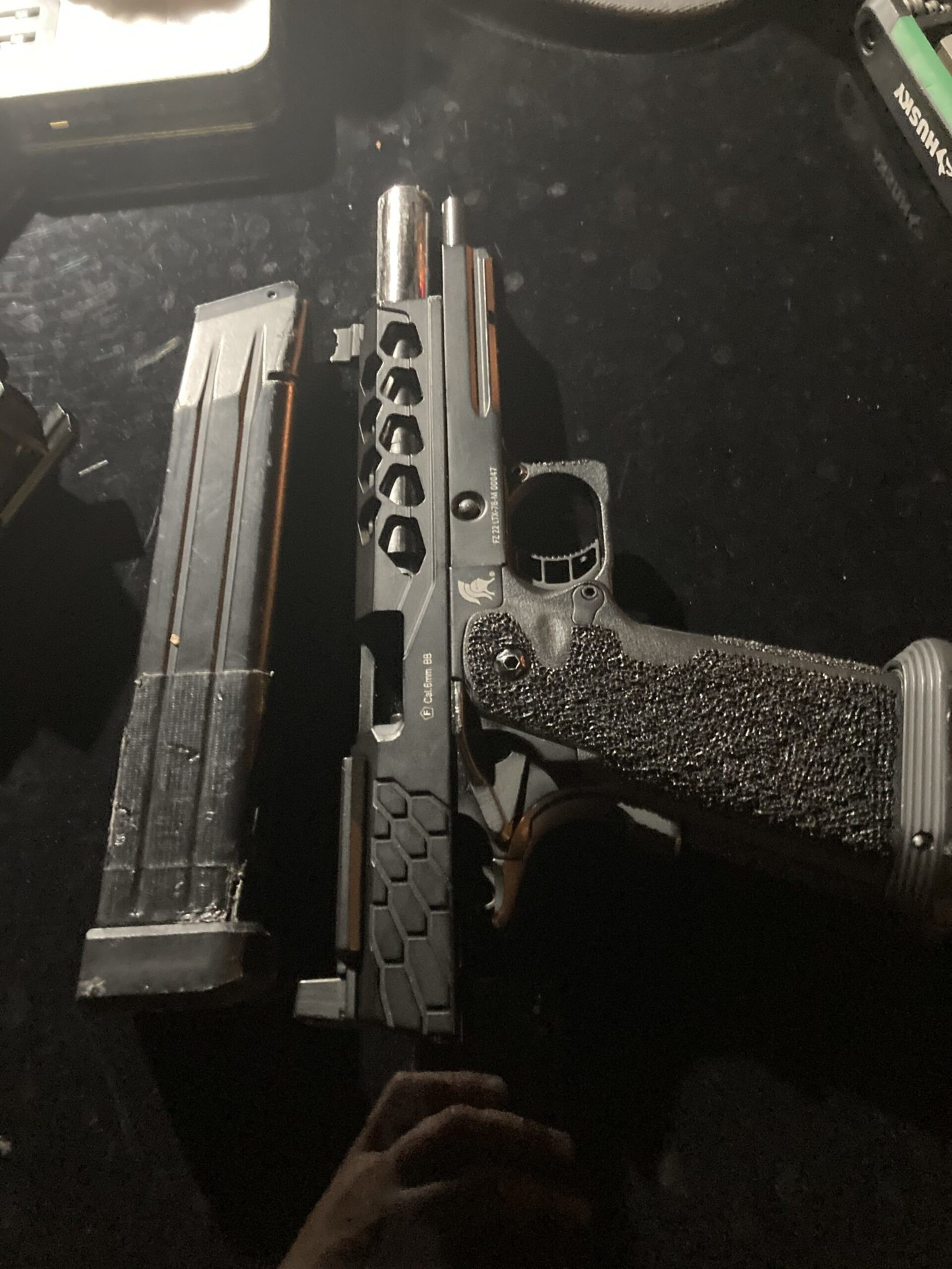 A black semi-automatic pistol with a textured grip lies next to a tall, black magazine on a dark surface.