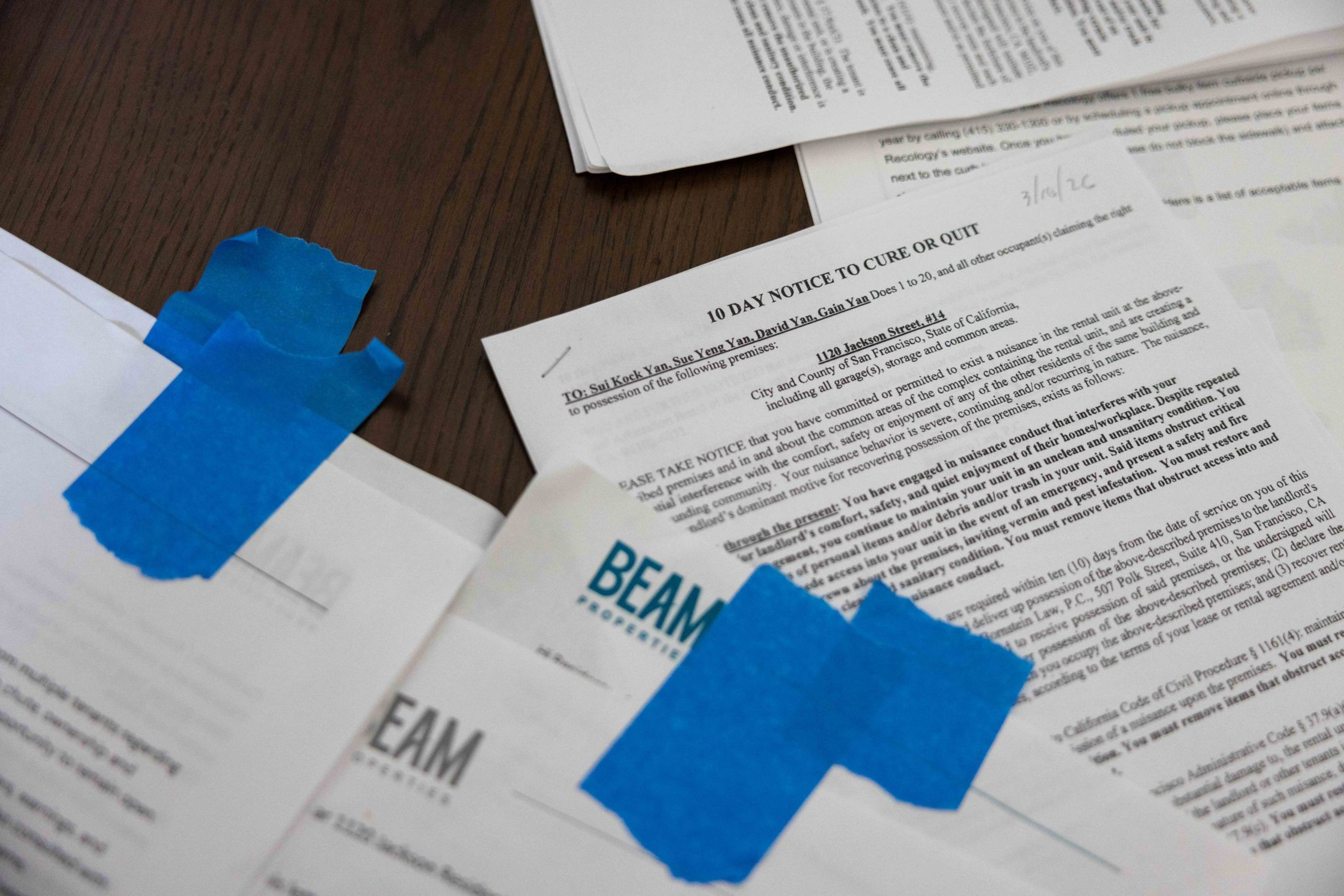 Several official papers, including a “10 Day Notice to Cure or Quit,” are taped with blue painter’s tape on a dark wooden surface.