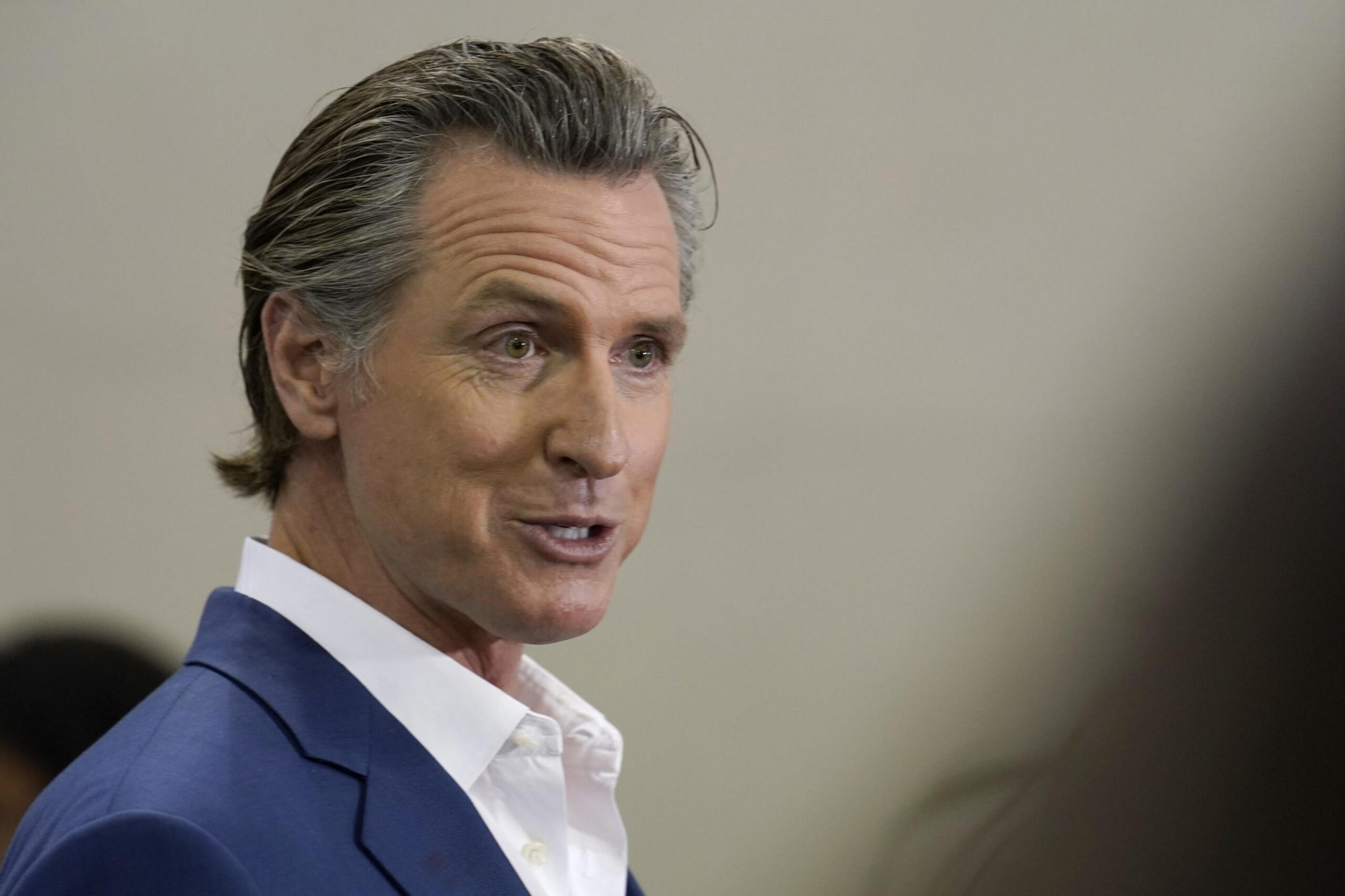 A man in a blue suit speaks, his expression earnest. His graying hair is slicked back.