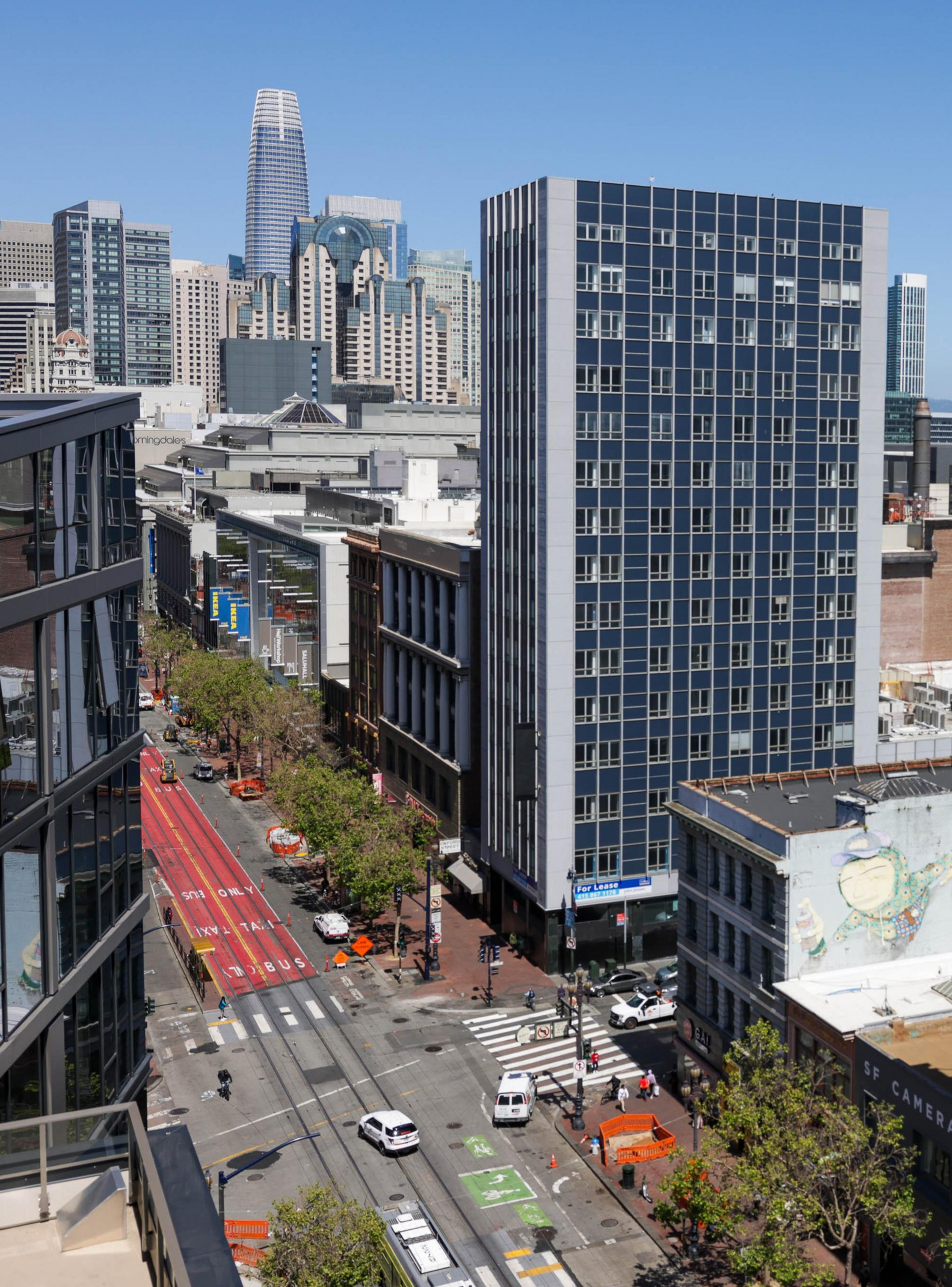 Aerial view of a city street with tall buildings, clear skies, and a few cars.