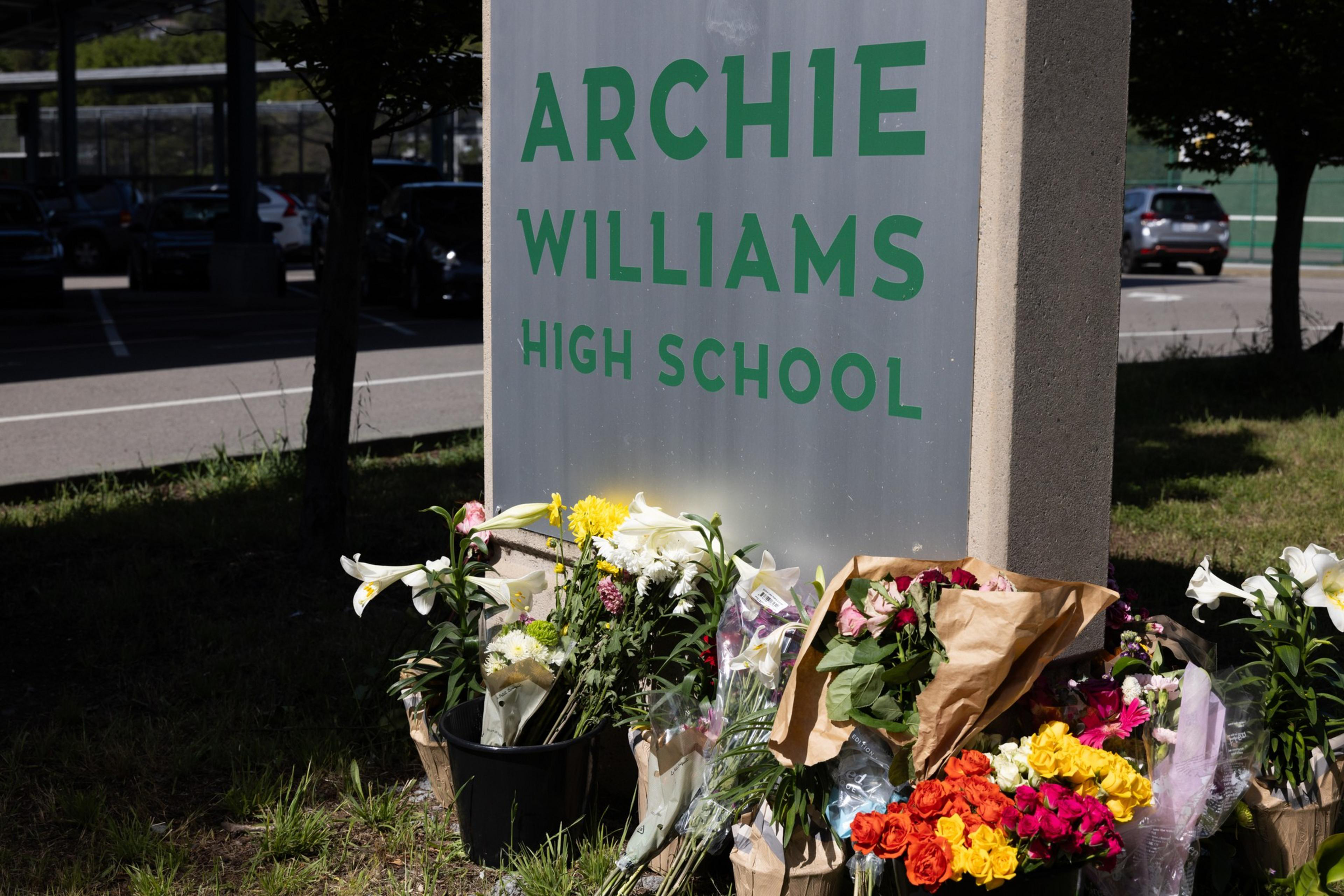 A sign reads "Archie Williams High School" with numerous floral tributes placed at its base, suggesting a memorial or tribute site.