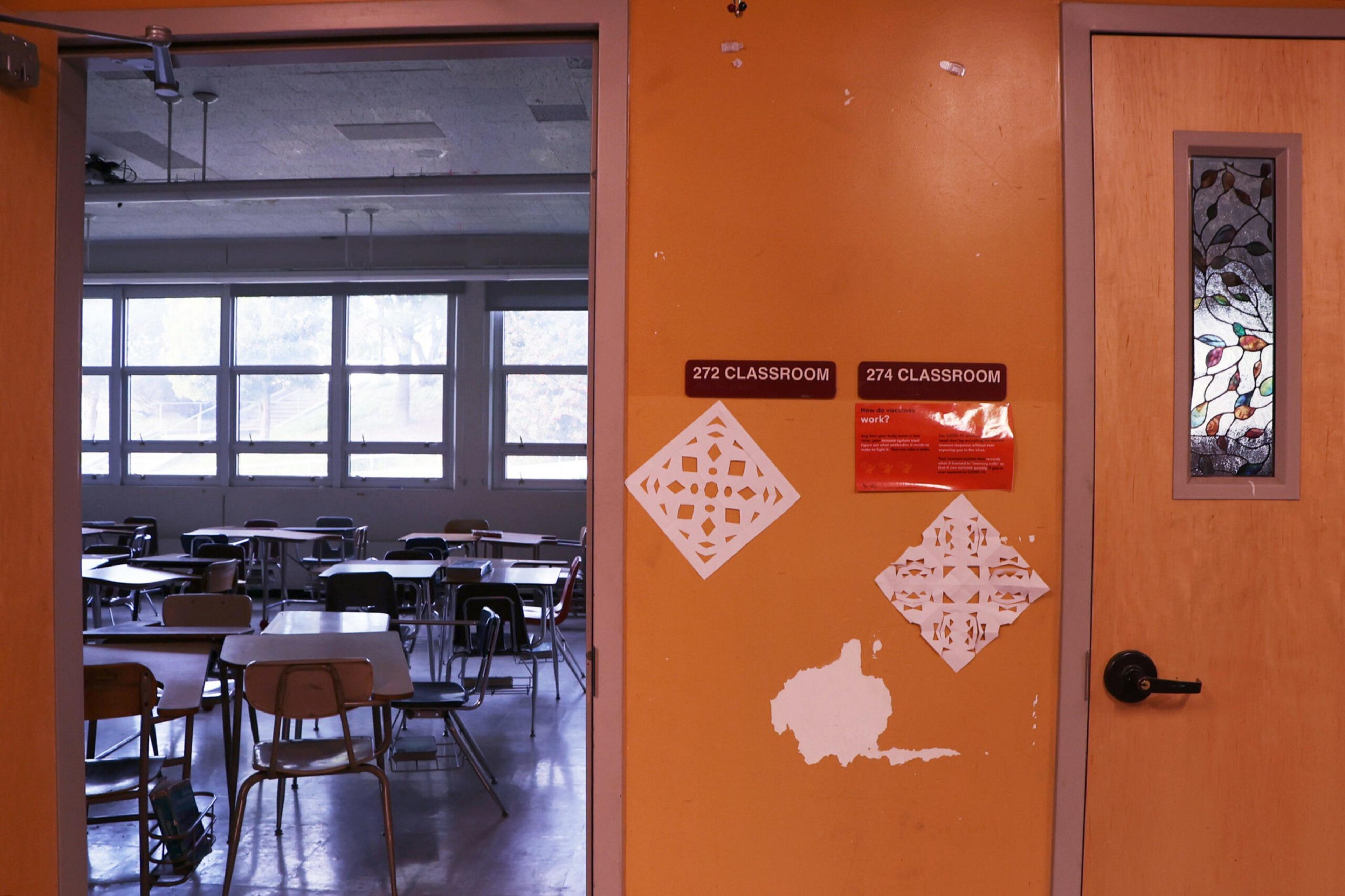 A classroom with empty desks and chairs is visible through an open door on an orange wall labeled 272 and 274 CLASSROOM, decorated with paper cutouts.