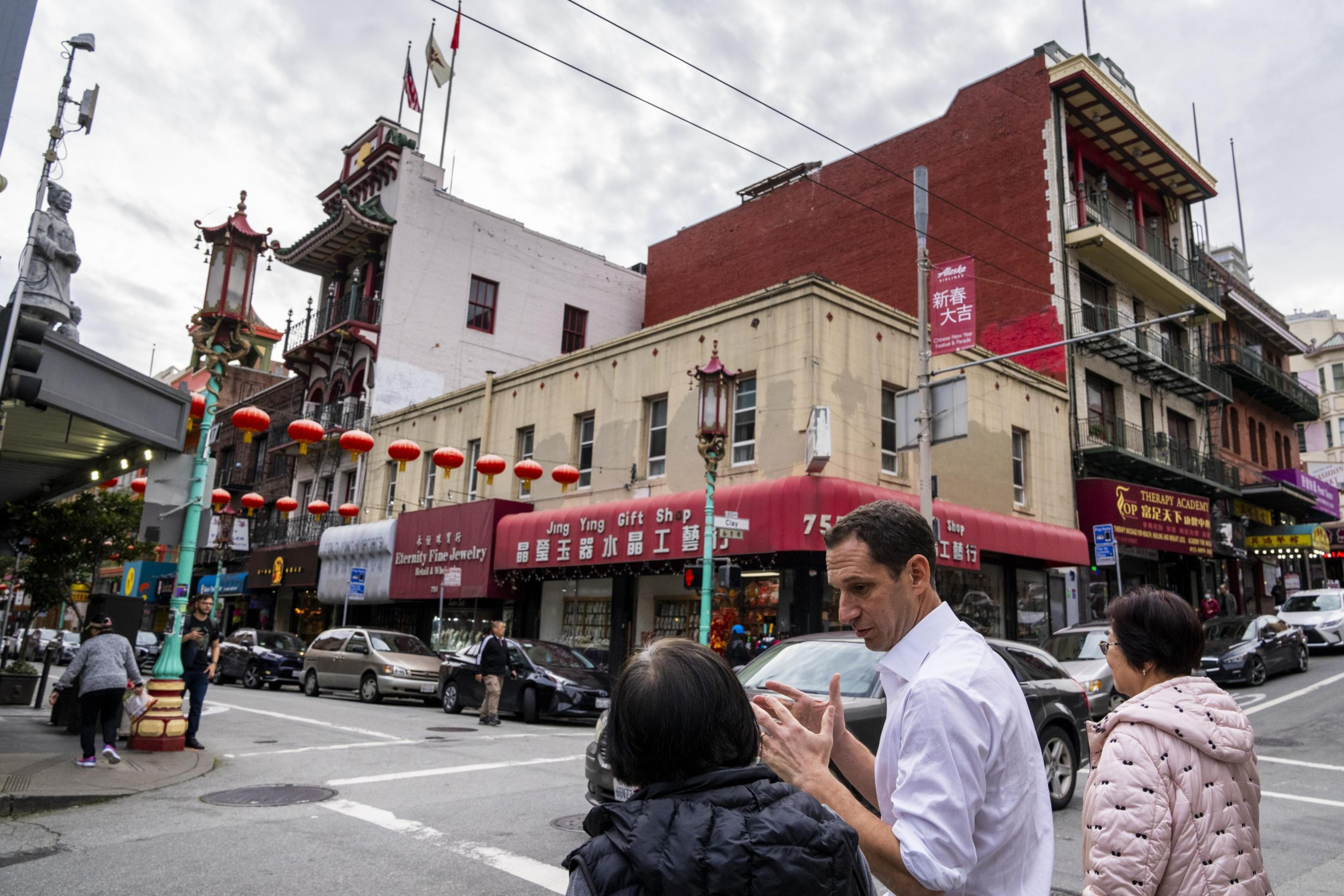 Street scene in Chinatown with lanterns, an ornate lamp post, and people talking.