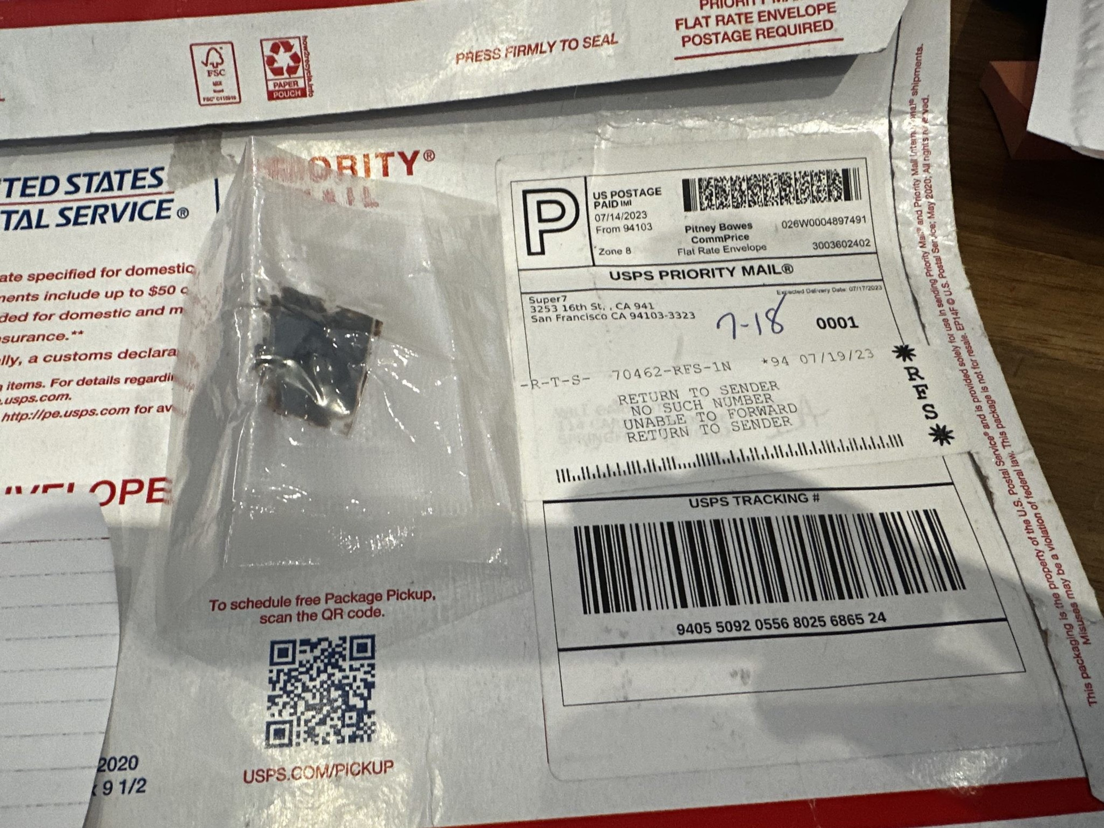 A USPS priority mail envelope lies open on a table. Inside, there's a small, clear plastic bag containing a tiny object. A printed label is visible.