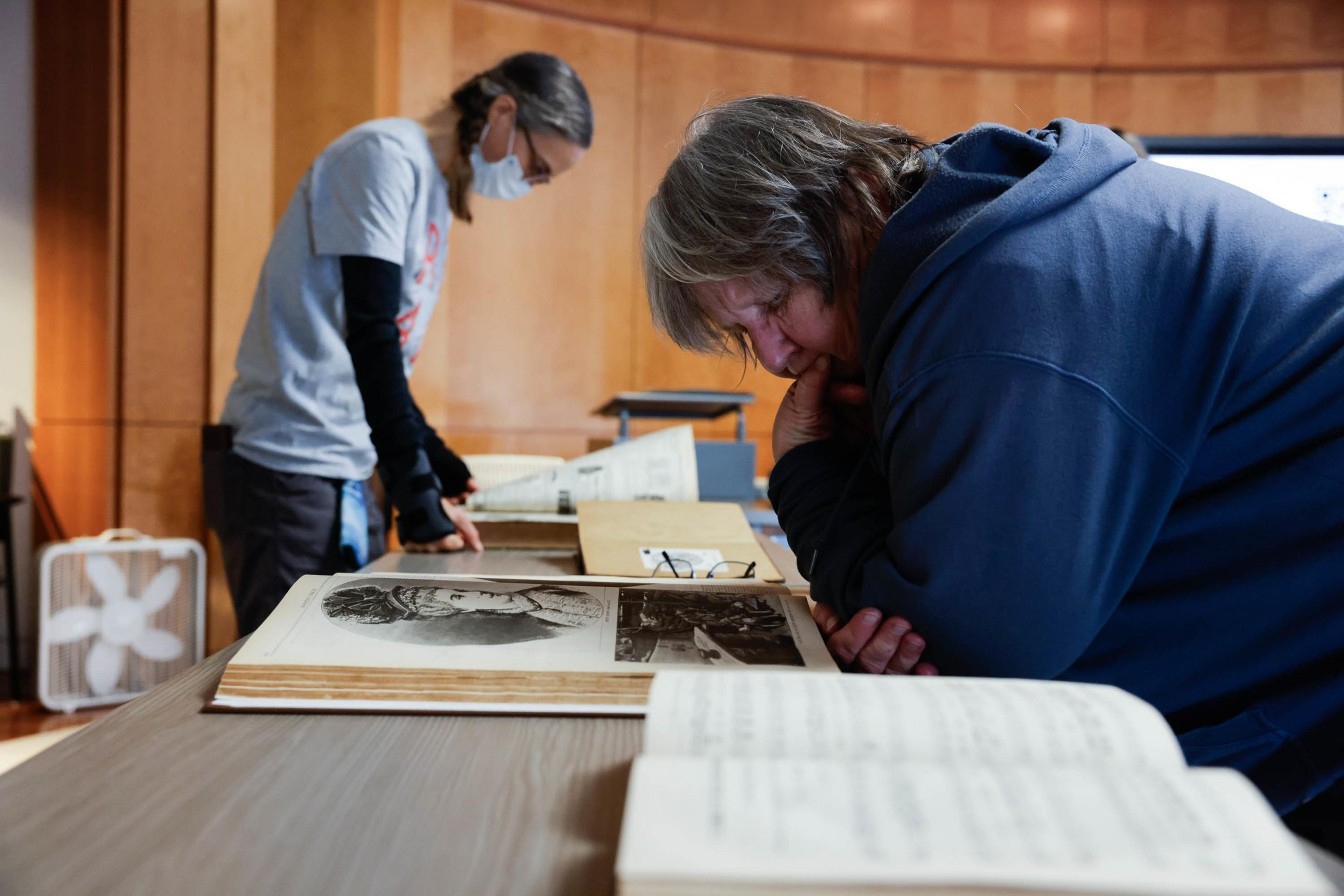 Two people examine old magazine s on a table; one is intently studying a page.