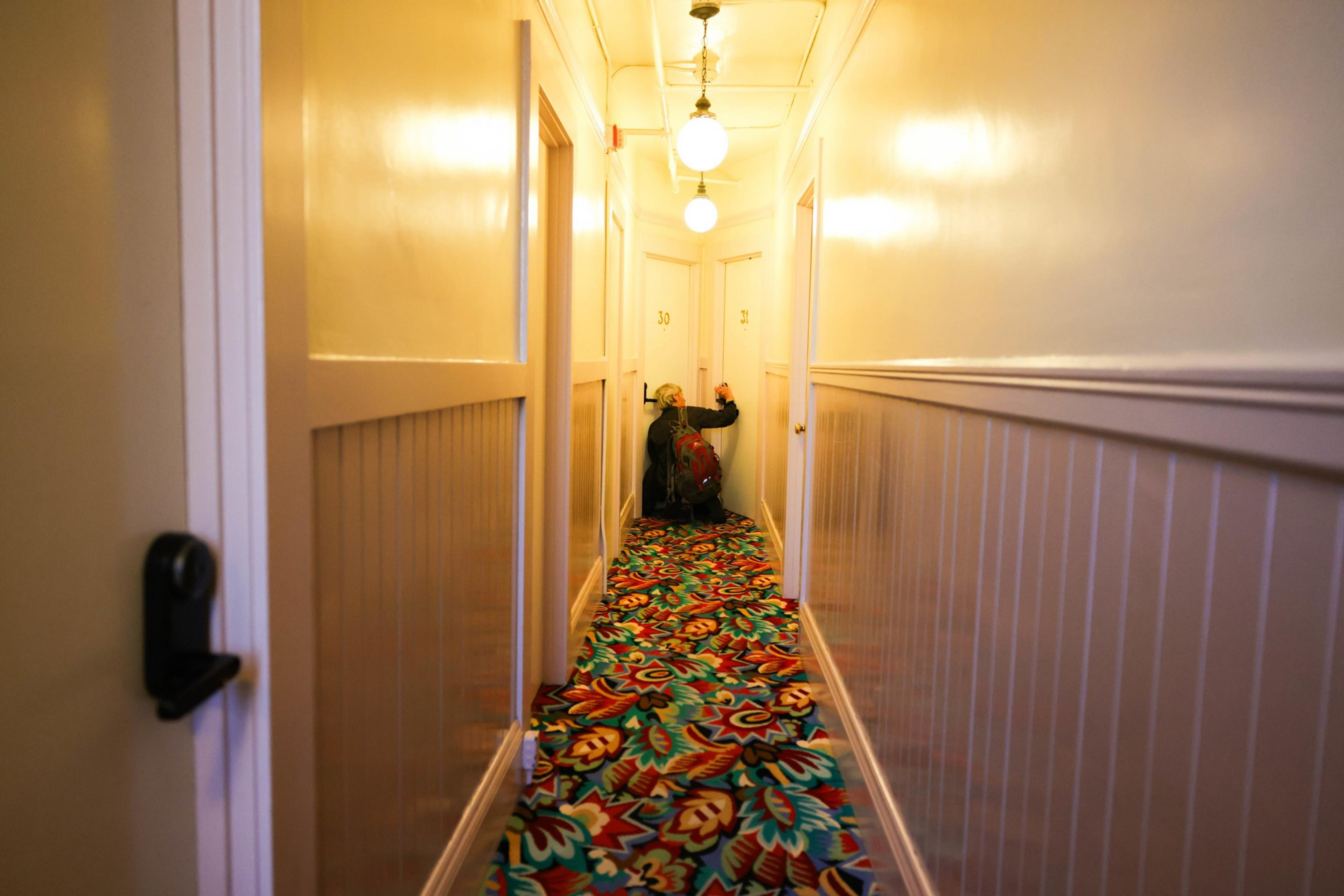 A person at the end of a hallway unlocking their door. 