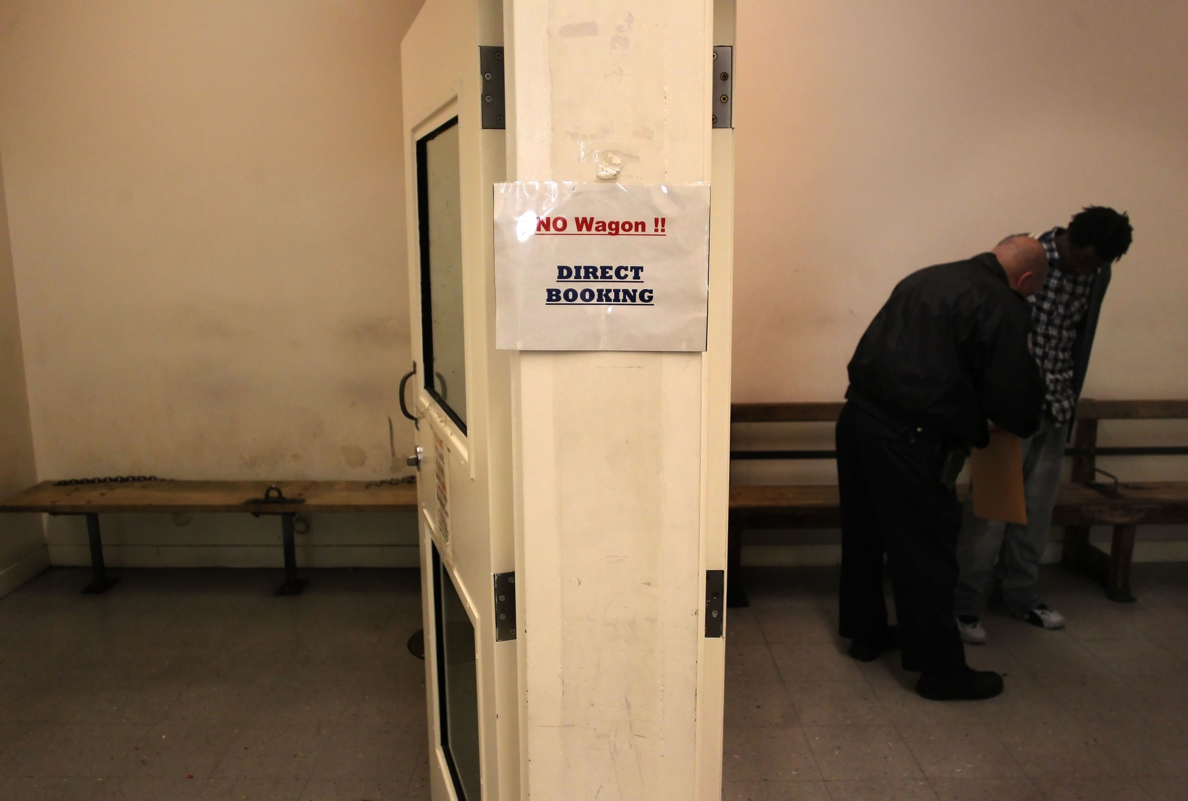A sign on a pillar reads "NO Wagon!! DIRECT BOOKING" with two men standing near benches in a sparse room.
