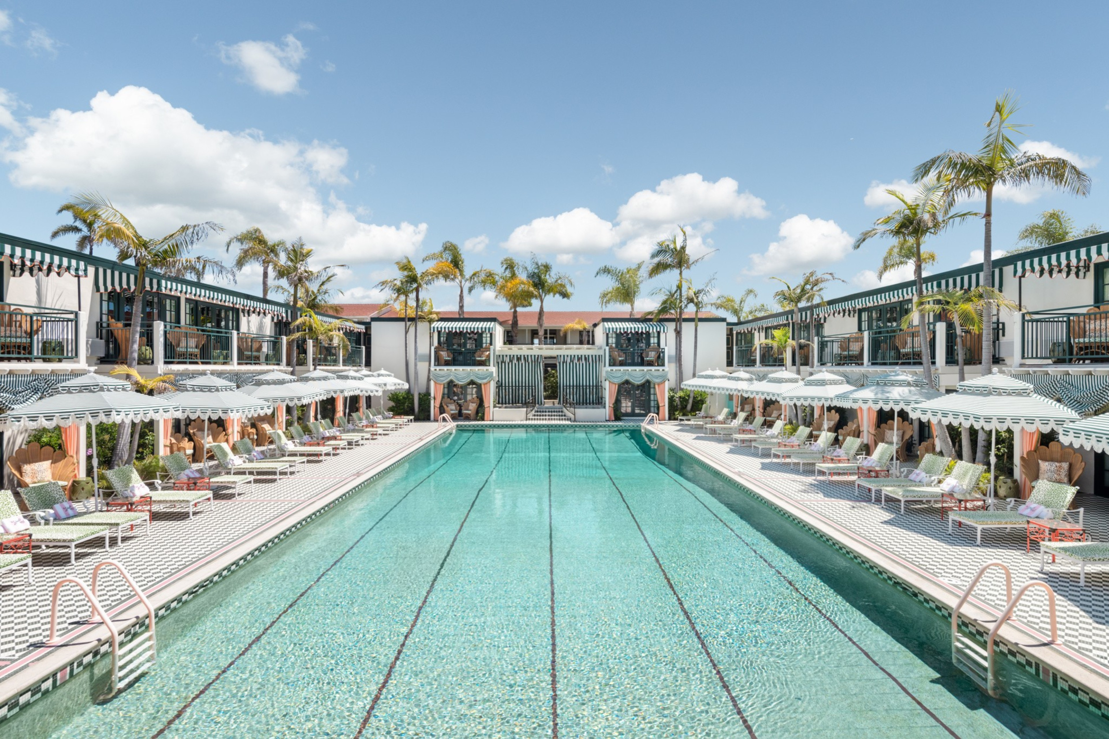 A large pool surrounded by lounge chairs umbrellas and palm trees