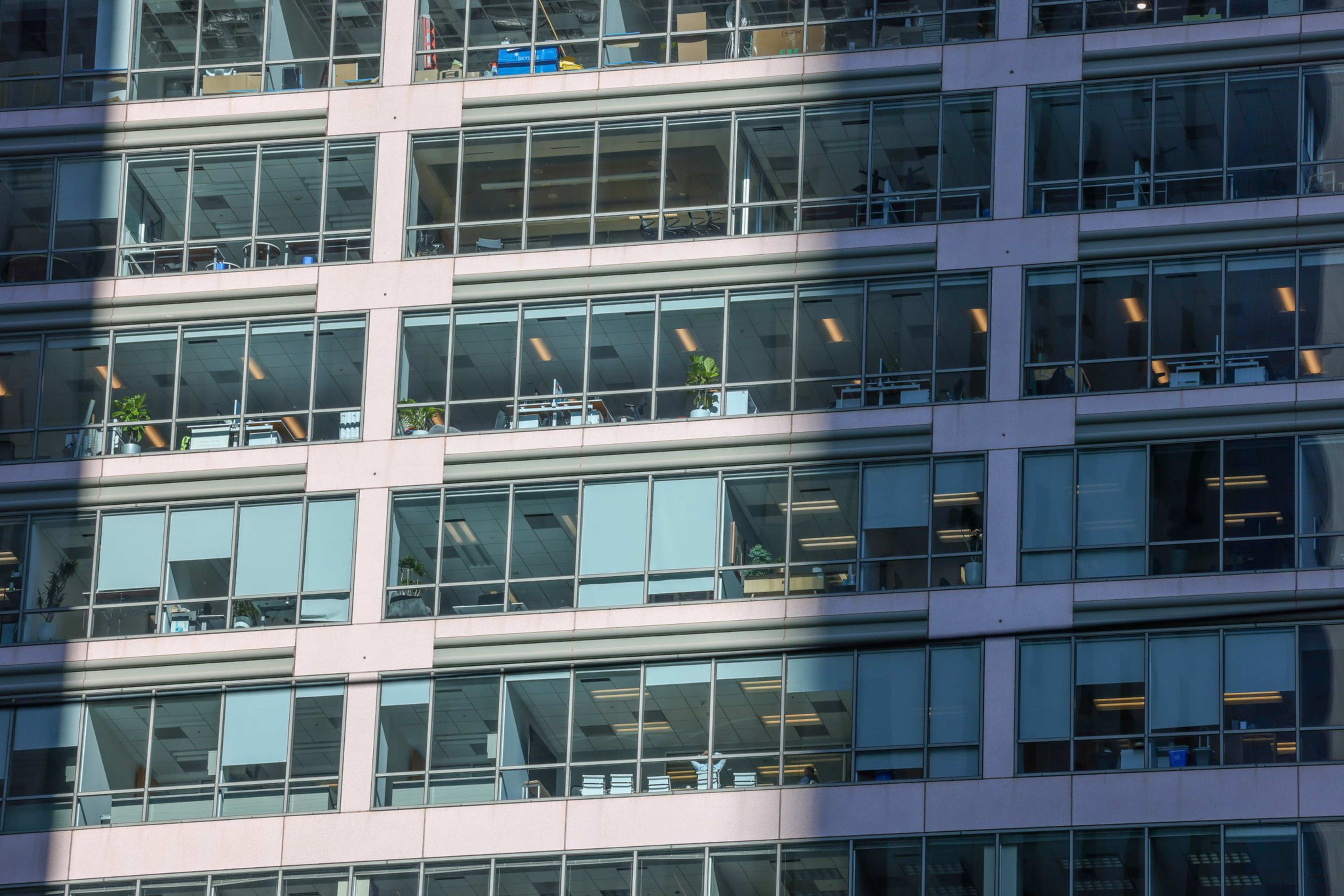 A close-up of a modern building's facade showing several floors with glass windows and office interiors.