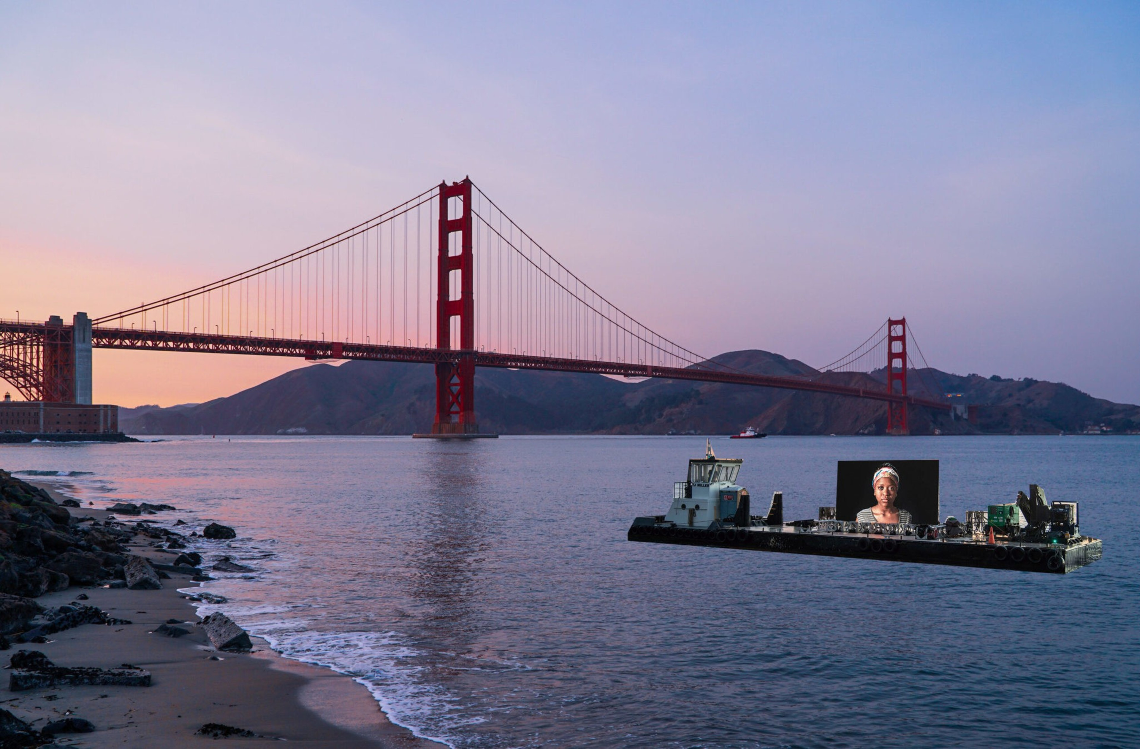 The Golden Gate Bridge spans across calm waters at sunset, while a boat with a large screen showing a woman's portrait floats nearby.