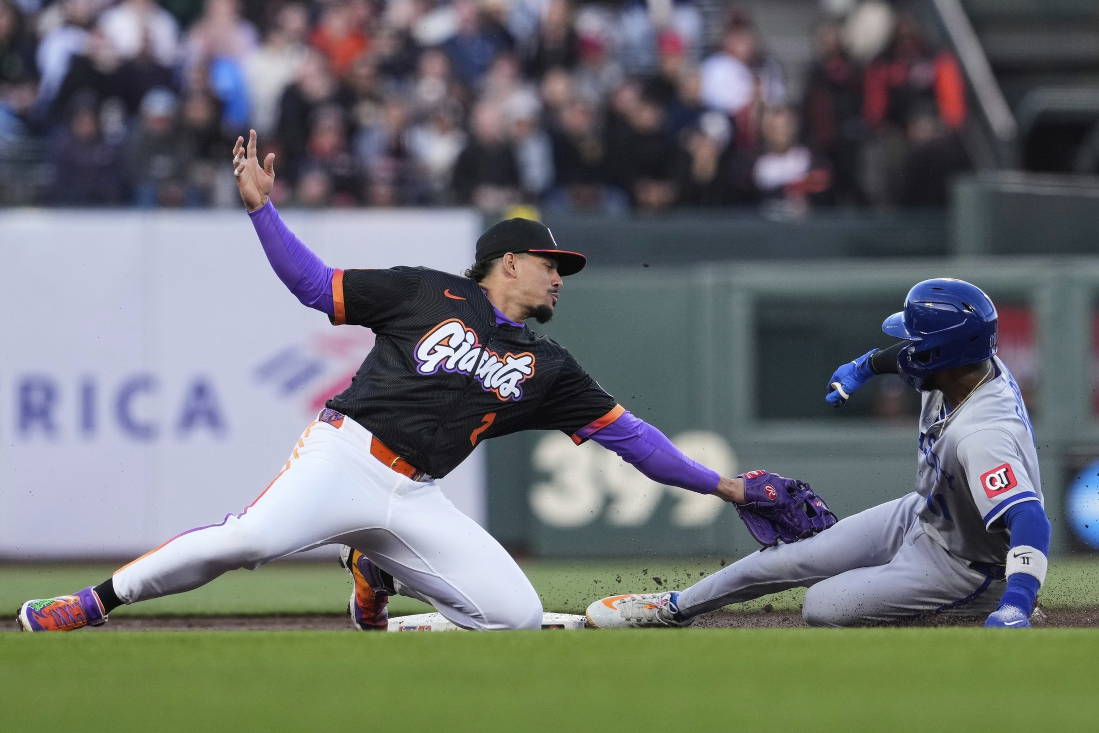 A baseball player in a black &quot;Giants&quot; uniform tags a sliding player in gray with blue helmet at a base. The focus is on the action and athleticism.