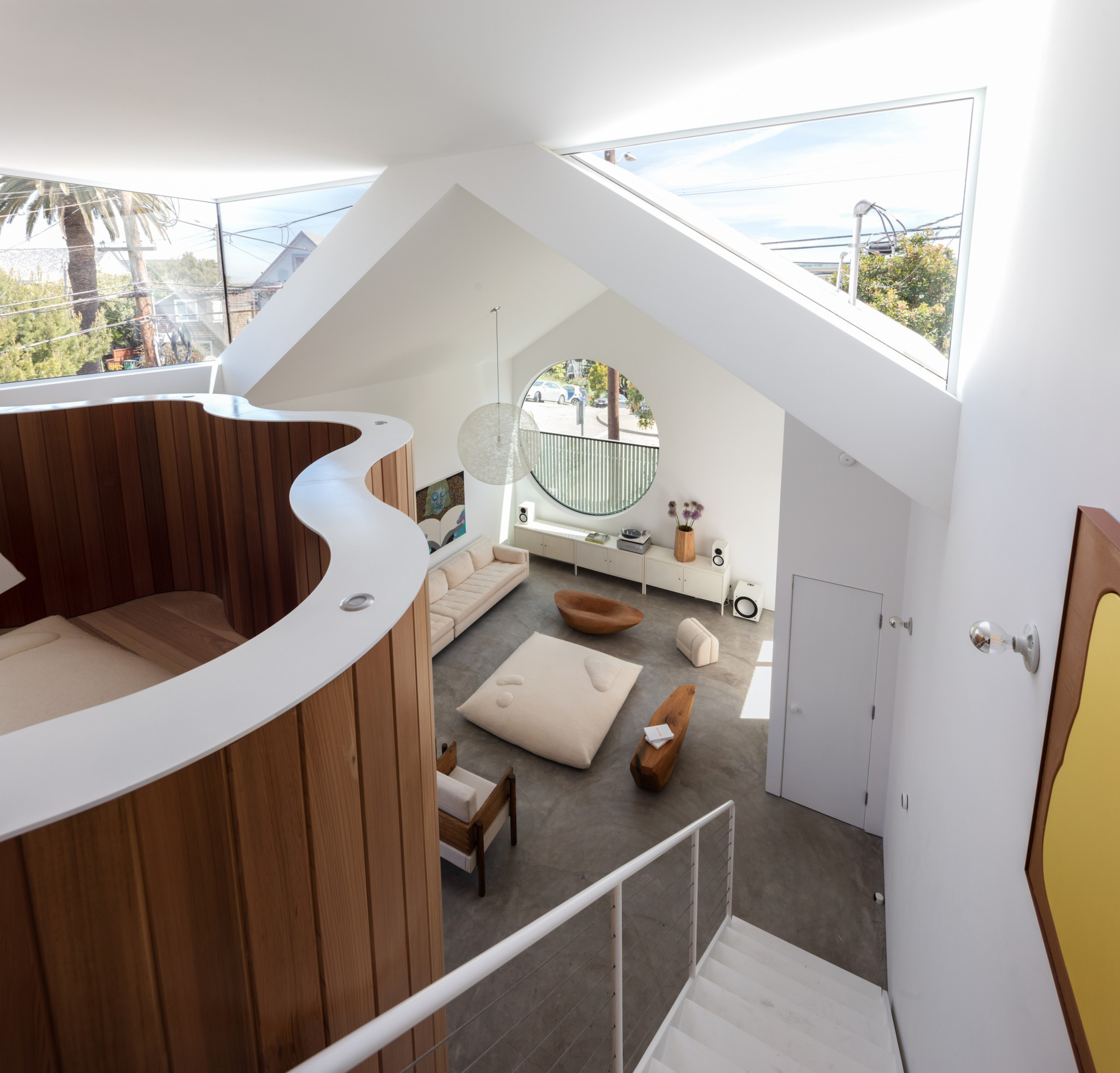 Modern loft-style room with wooden accents, large windows, unique curved structures, and minimalist furniture. Bright space with a view of the outside.