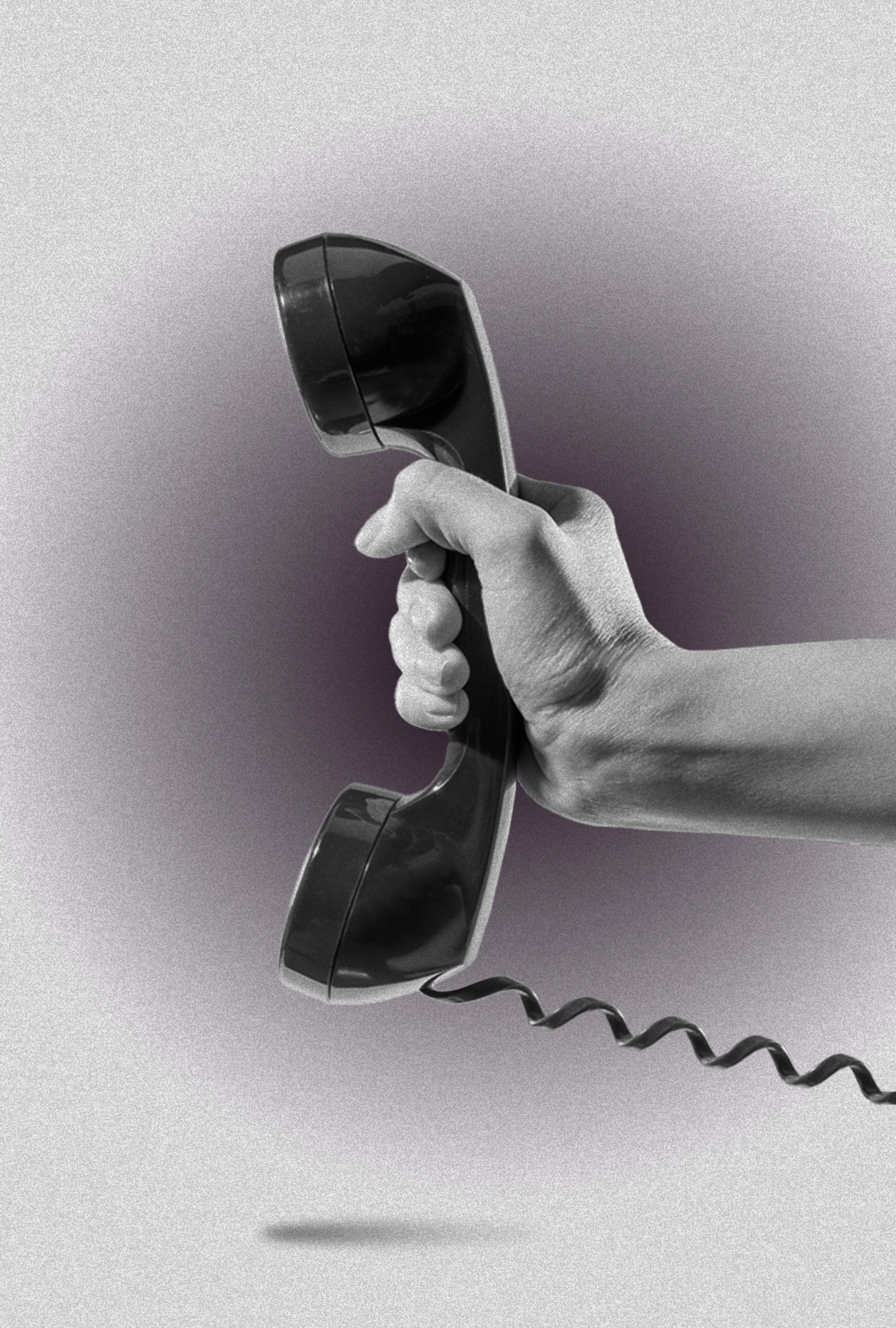 A hand tightly grips a black, corded telephone receiver against a gray background, with the cord dangling loosely below.