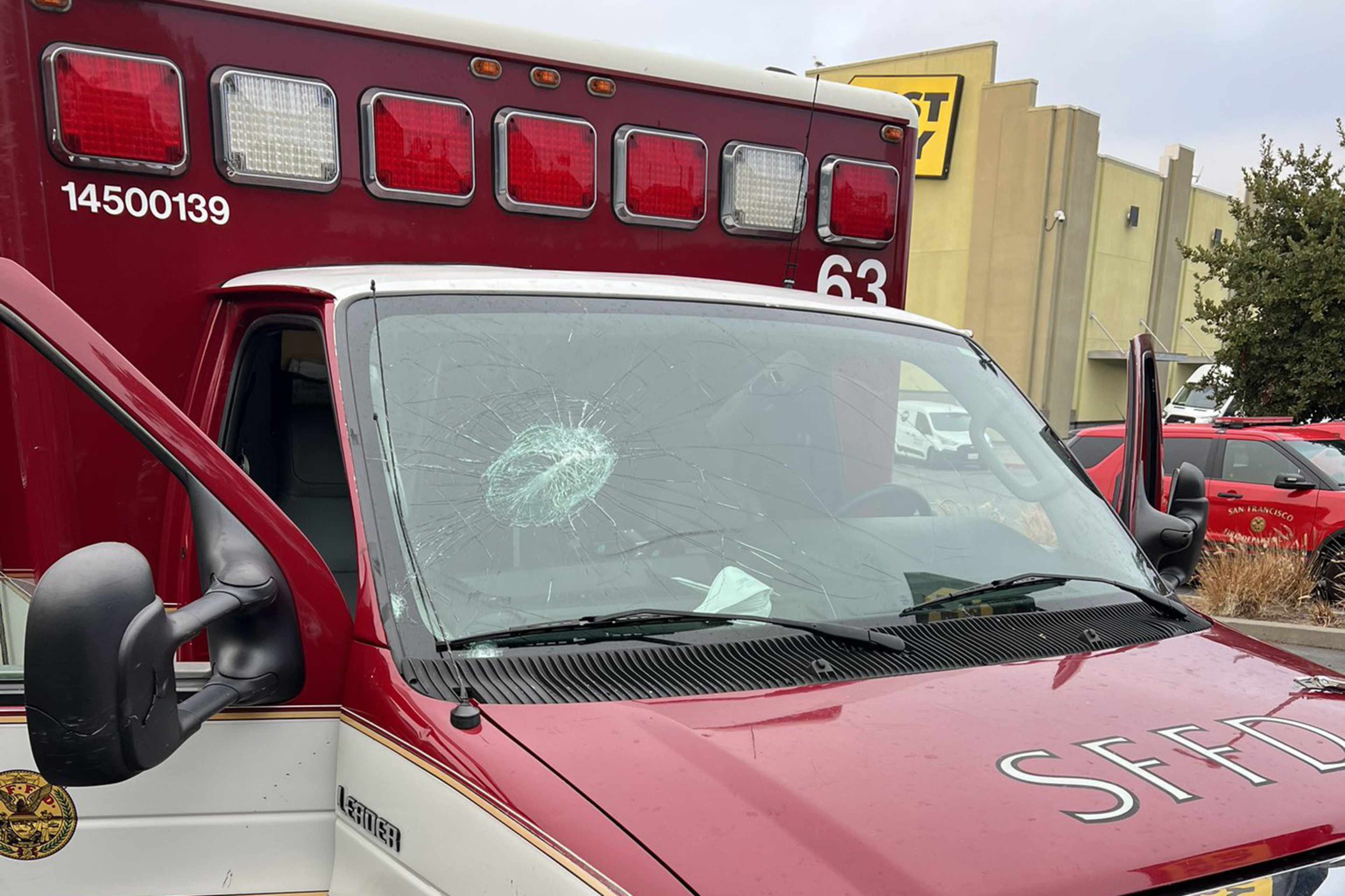 A red and white emergency vehicle with "SFFD" on the hood has a shattered windshield with a large circular crack near the center.