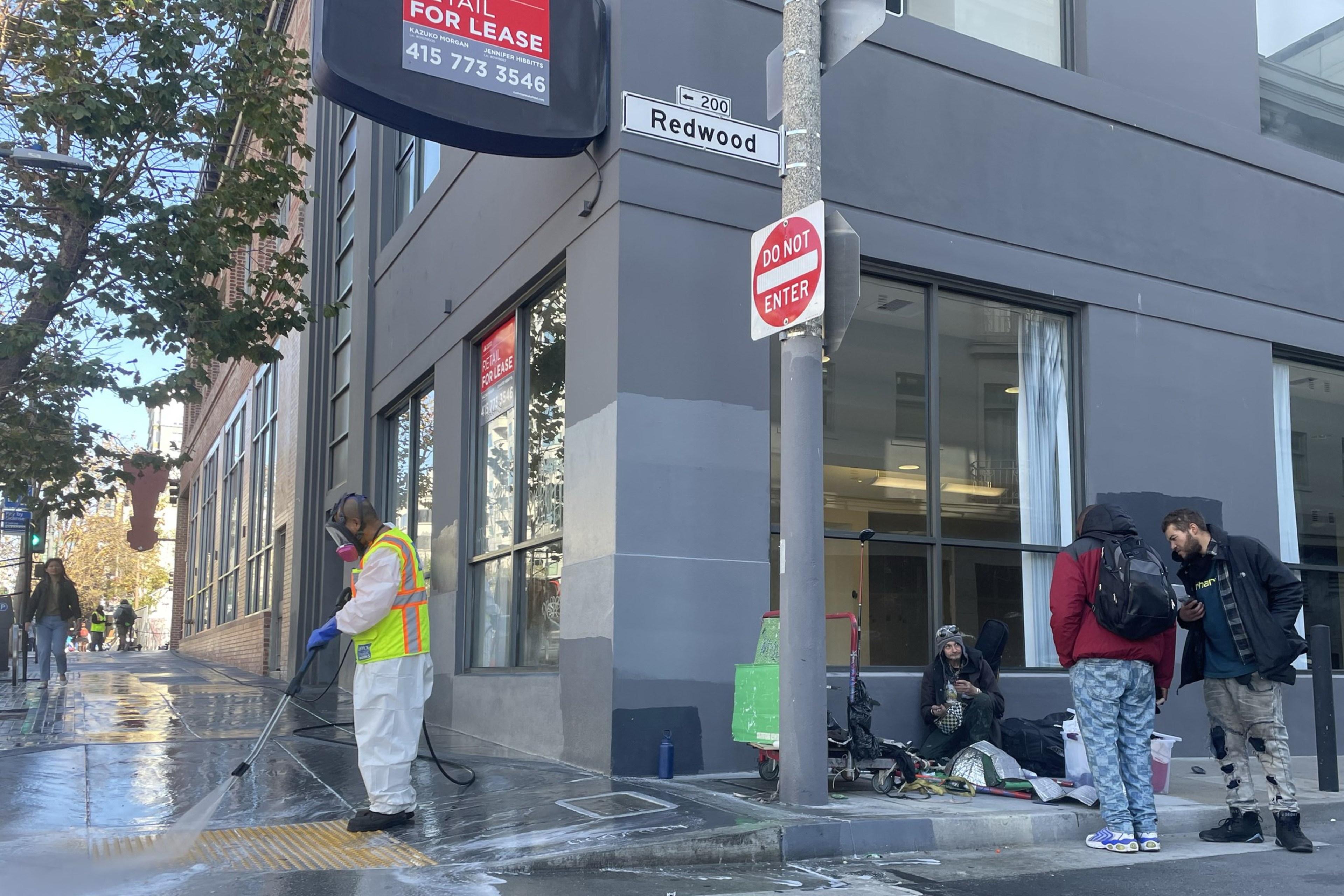A worker power washes the ground as 3 people while sitting and standing a few feet away.