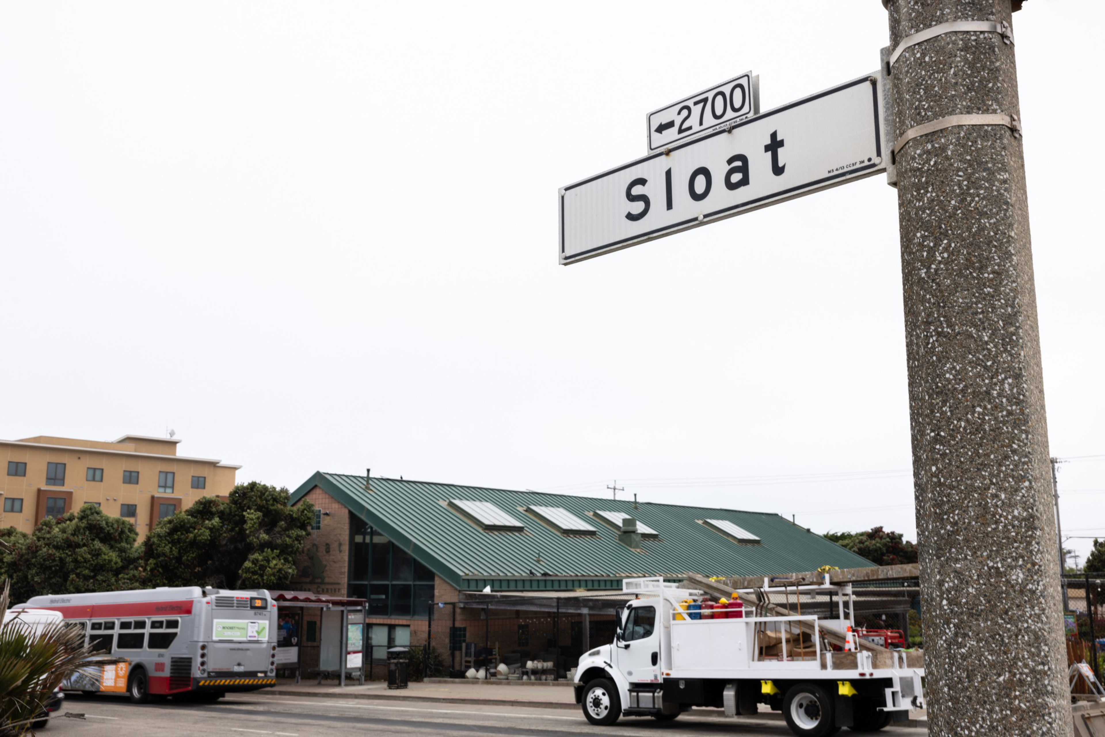 A street sign reads "Sloat 2700" next to a textured pole. Below, a bus and a white truck are parked in front of a green-roofed building.