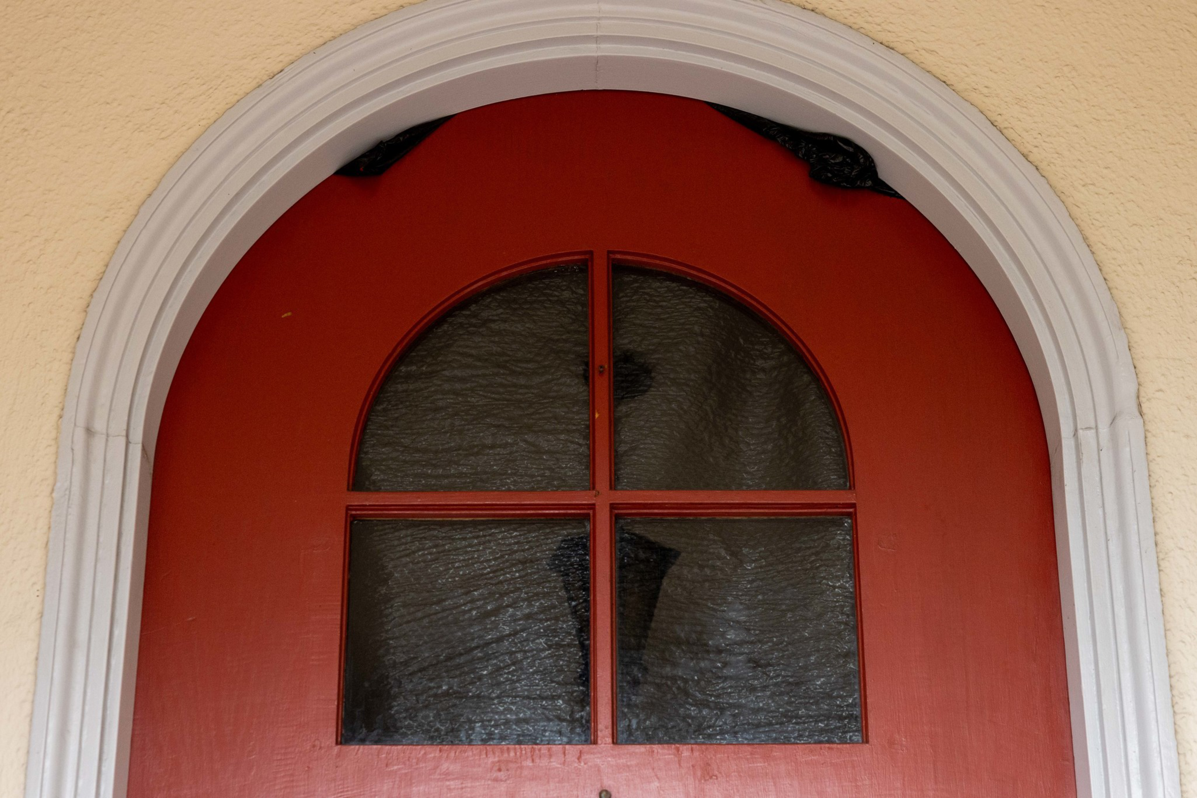A red arched door with four textured glass window panes and a white curved trim around the top and sides is set in a beige wall.
