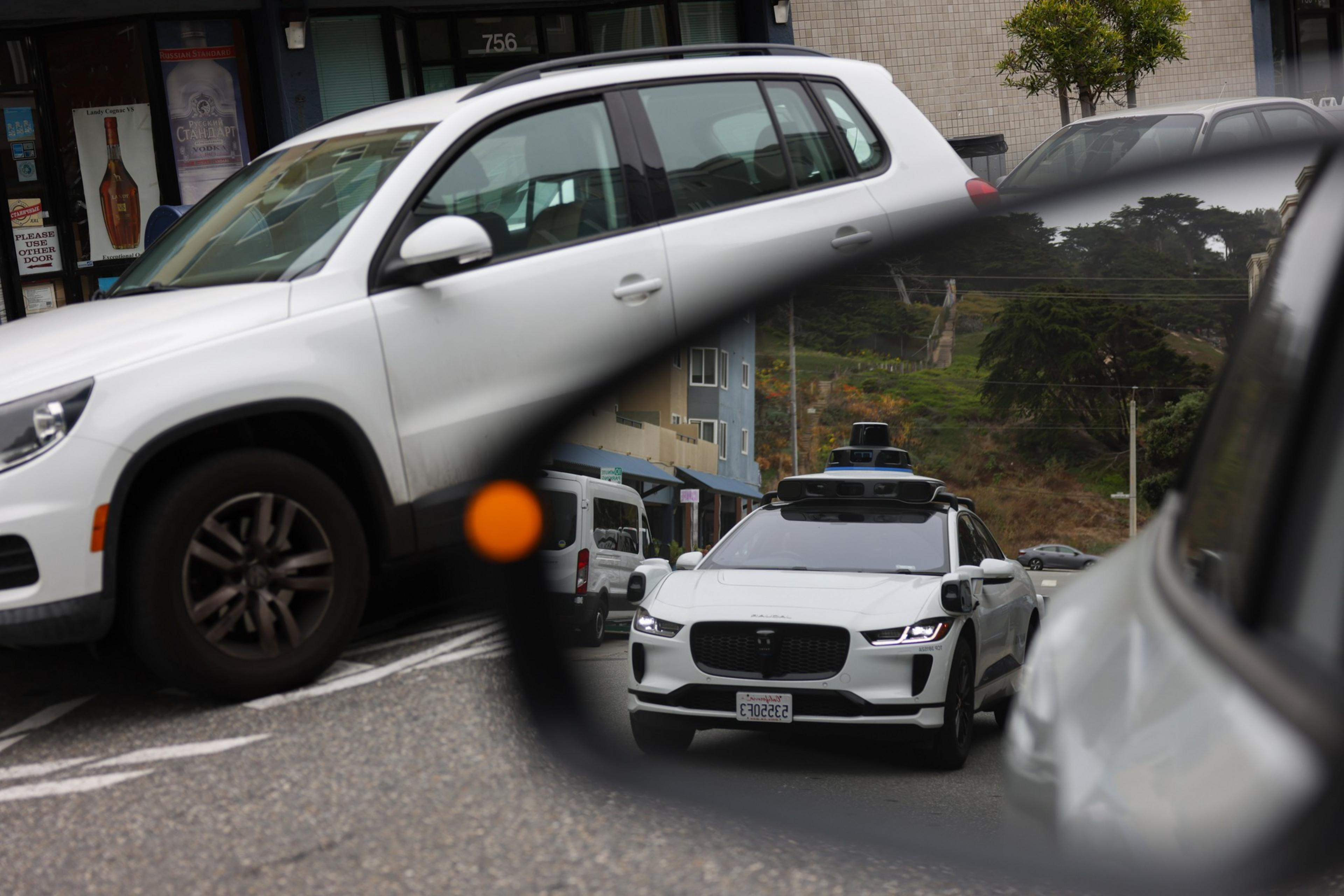 A driverless car is seen reflected in a car rearview window.