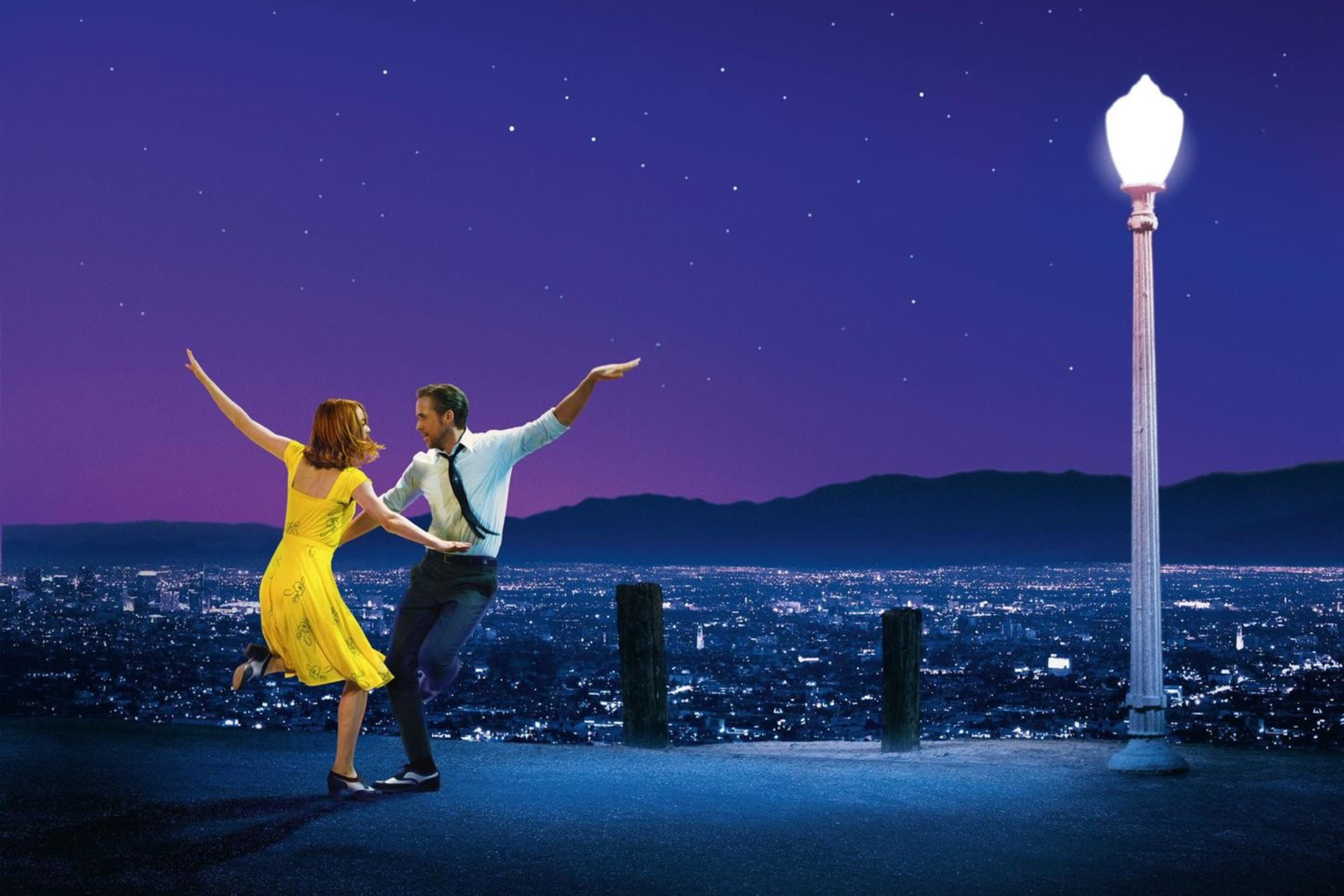 A couple dances joyfully on a hilltop at night, with city lights below, a starry sky above, and a single glowing streetlamp nearby.